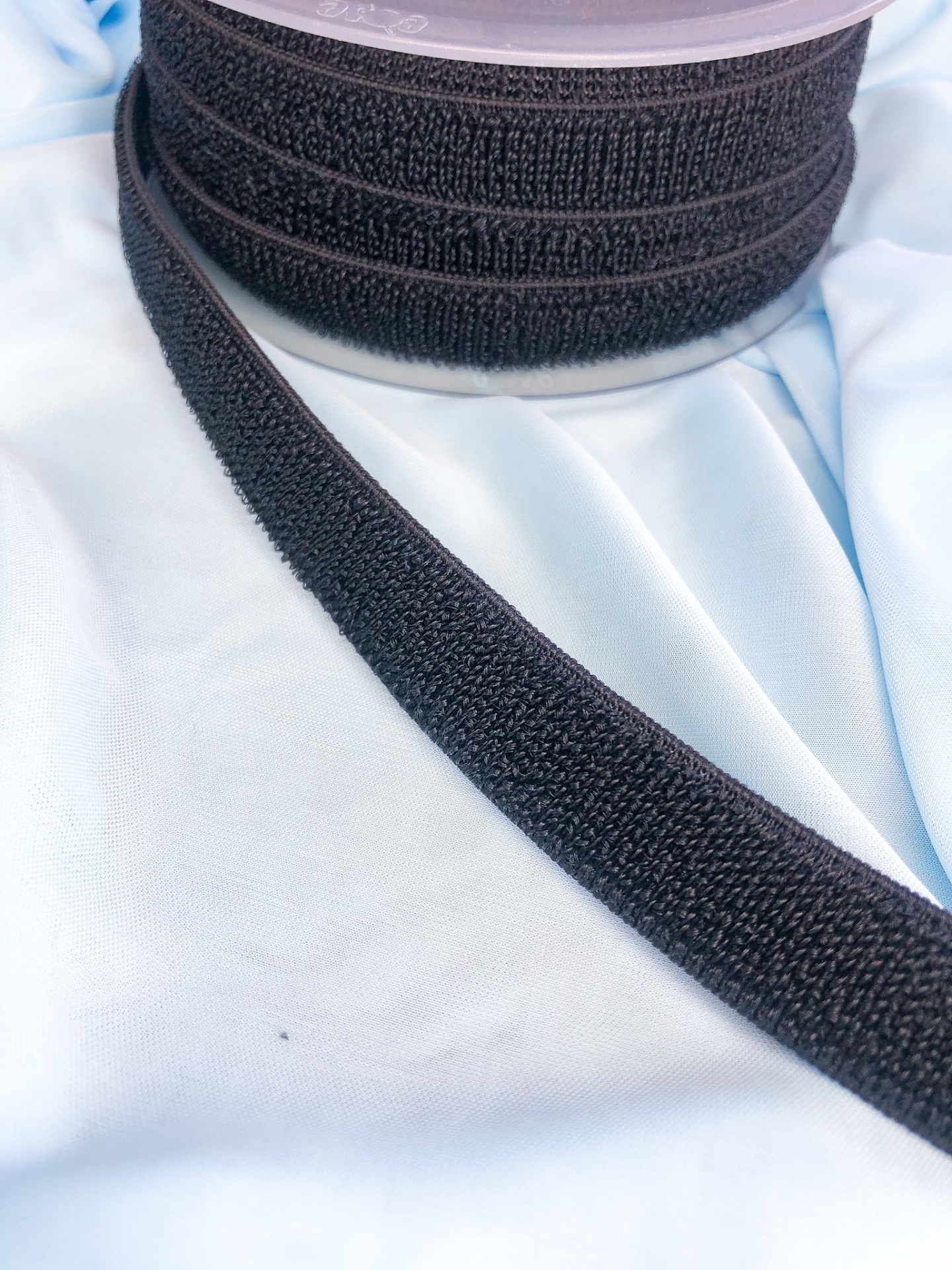 Rolo de fita adesiva preta tipo velcro sobre tecido azul claro