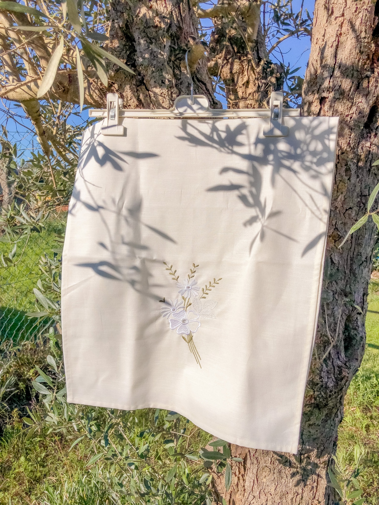 Pano branco com bordado floral pendurado numa árvore ao ar livre