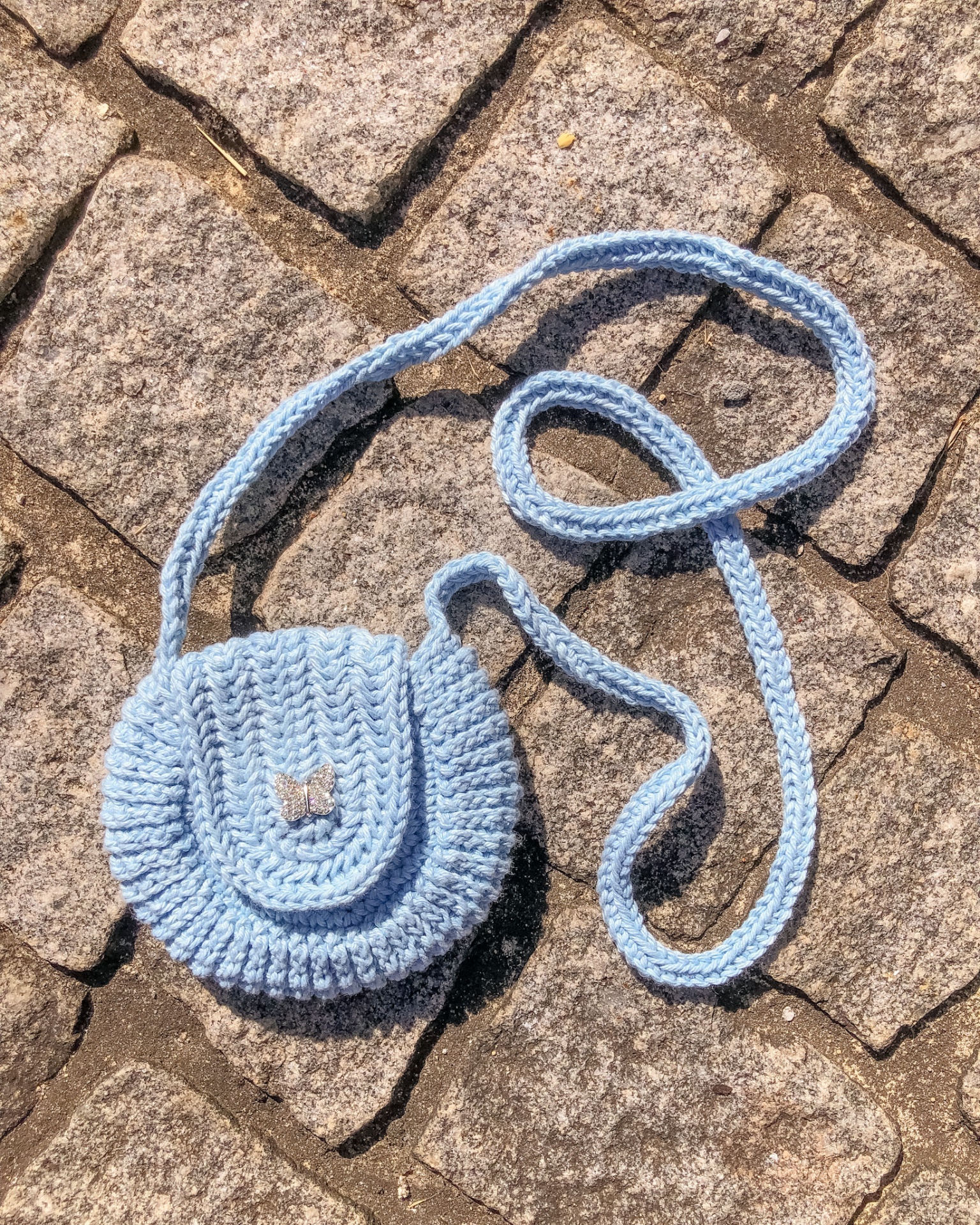 Mala pequena azul de croche com alça sobre chão de pedras cinzentas
