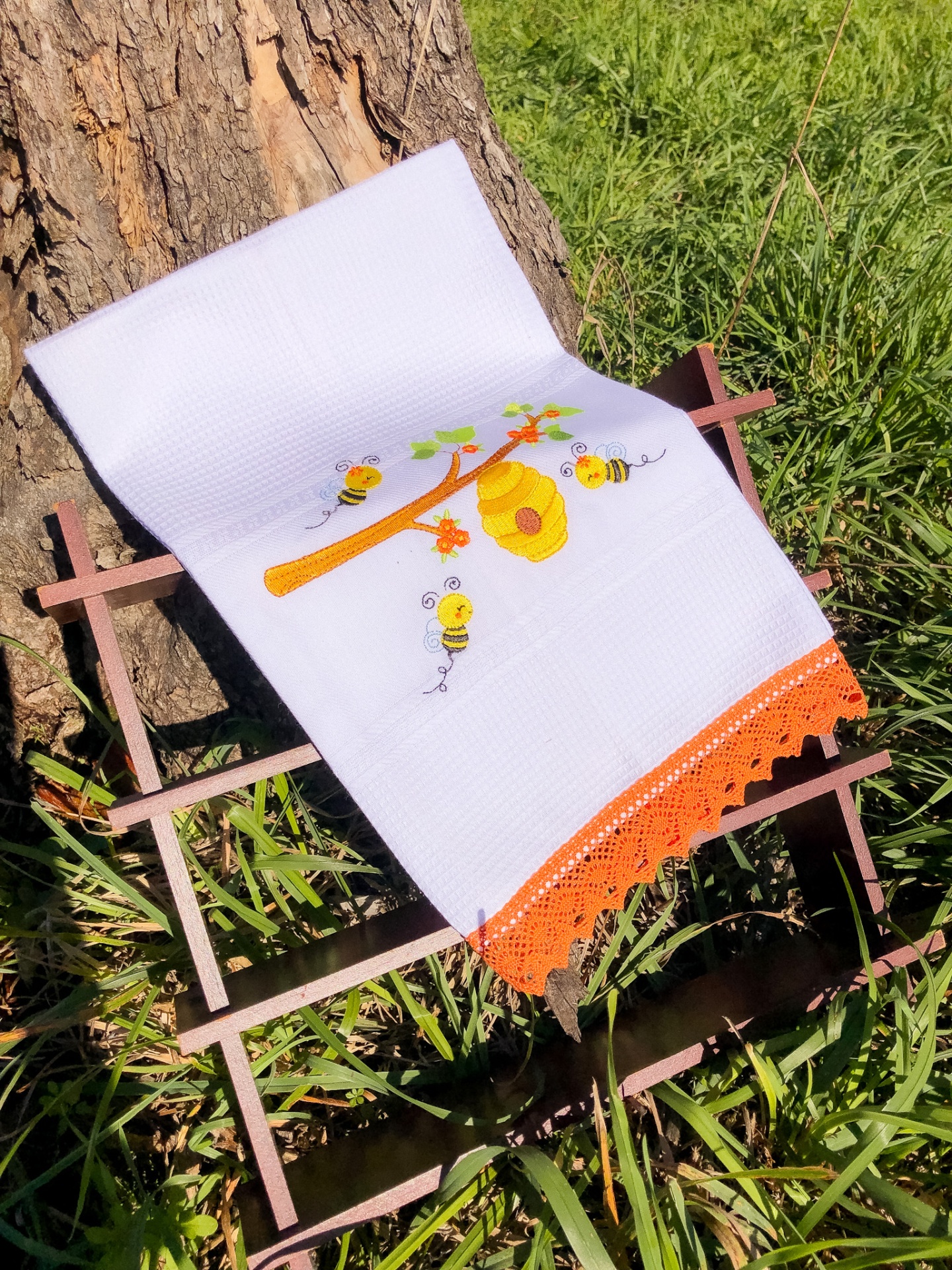 Toalha branca bordada com tema de abelhas e colmeia com barra de crochê laranja.