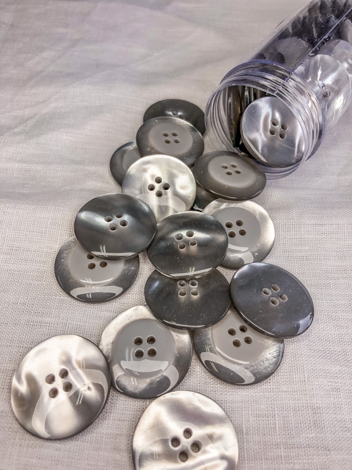 Botões redondos cinzentos e brancos com quatro furos e frasco plástico transparente aberto