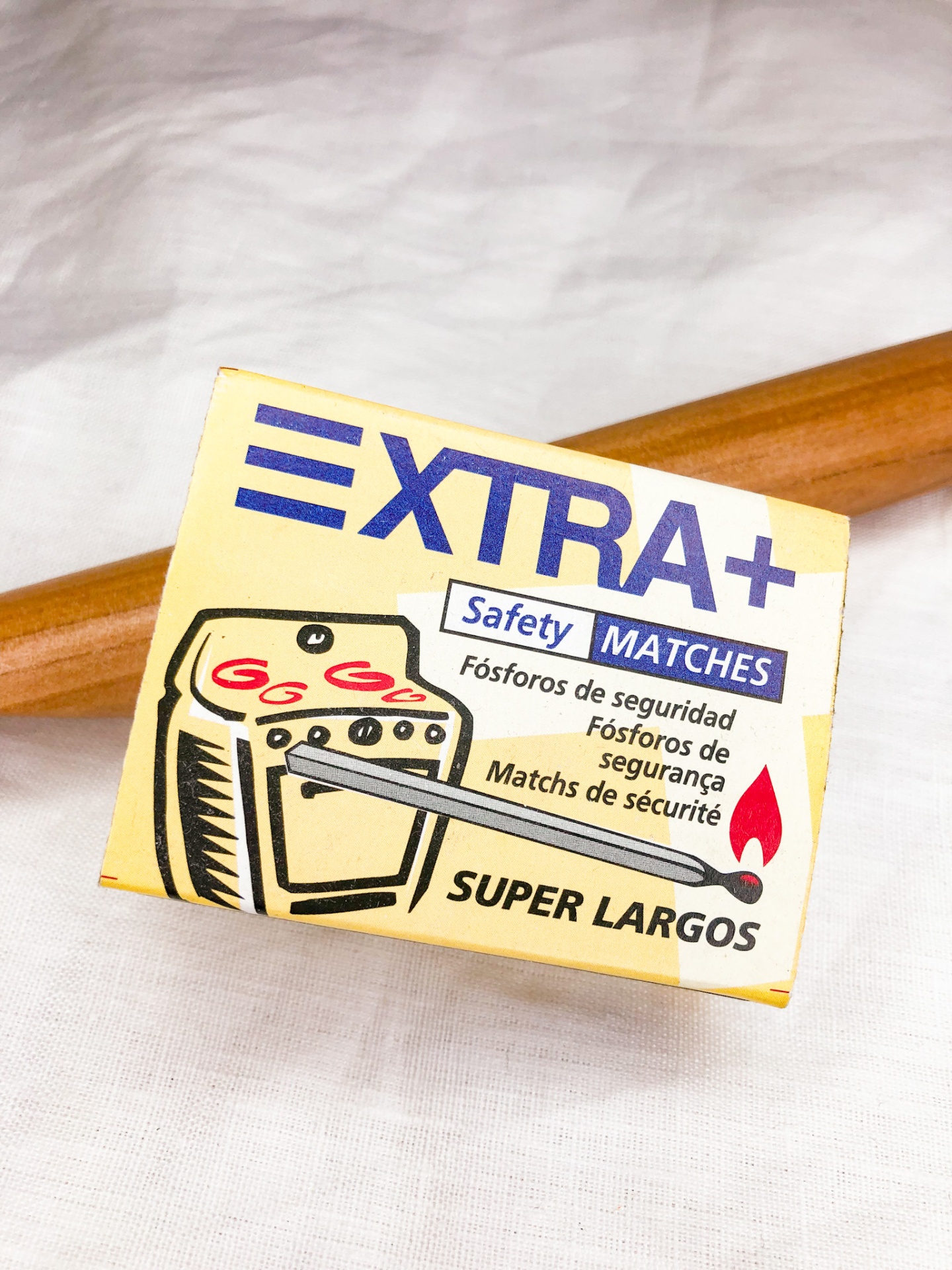 Caixa amarela de fósforos Extra+ com fósforo aceso e texto em várias línguas