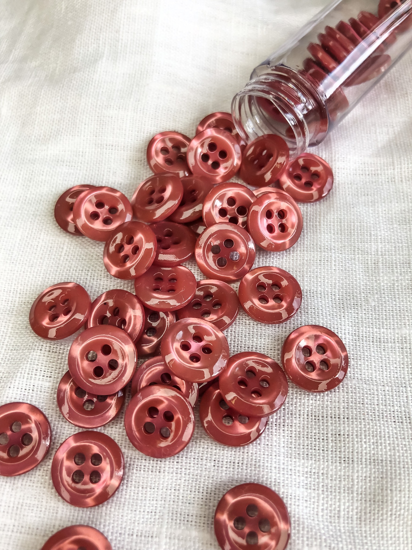 Botões vermelhos de plástico com quatro furos sobre tecido branco e tubo plástico aberto