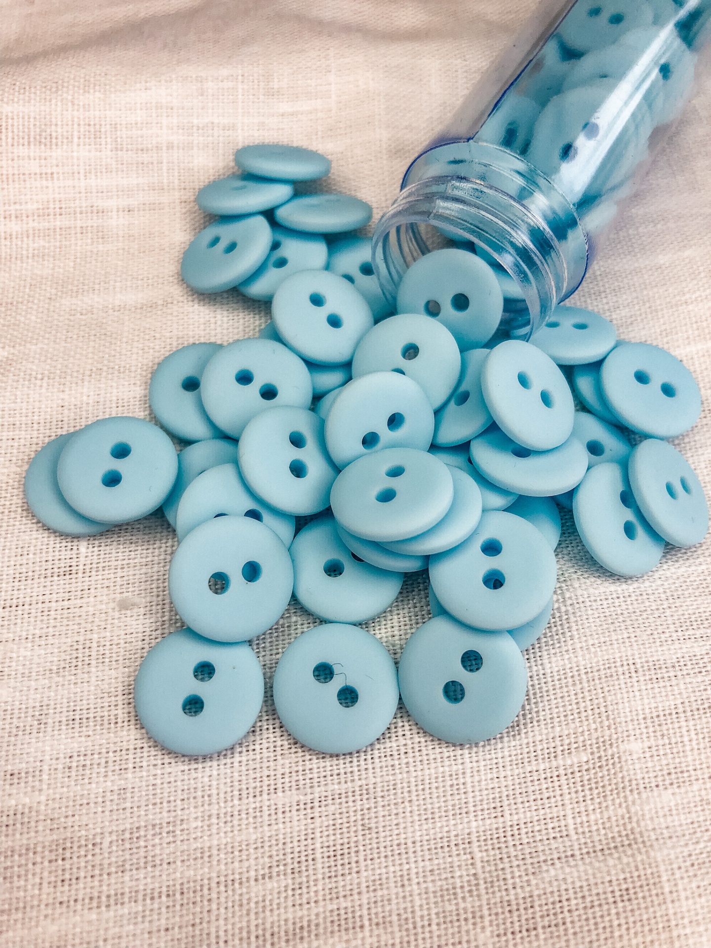Botões redondos azuis claros com dois furos próximos a um frasco transparente azul