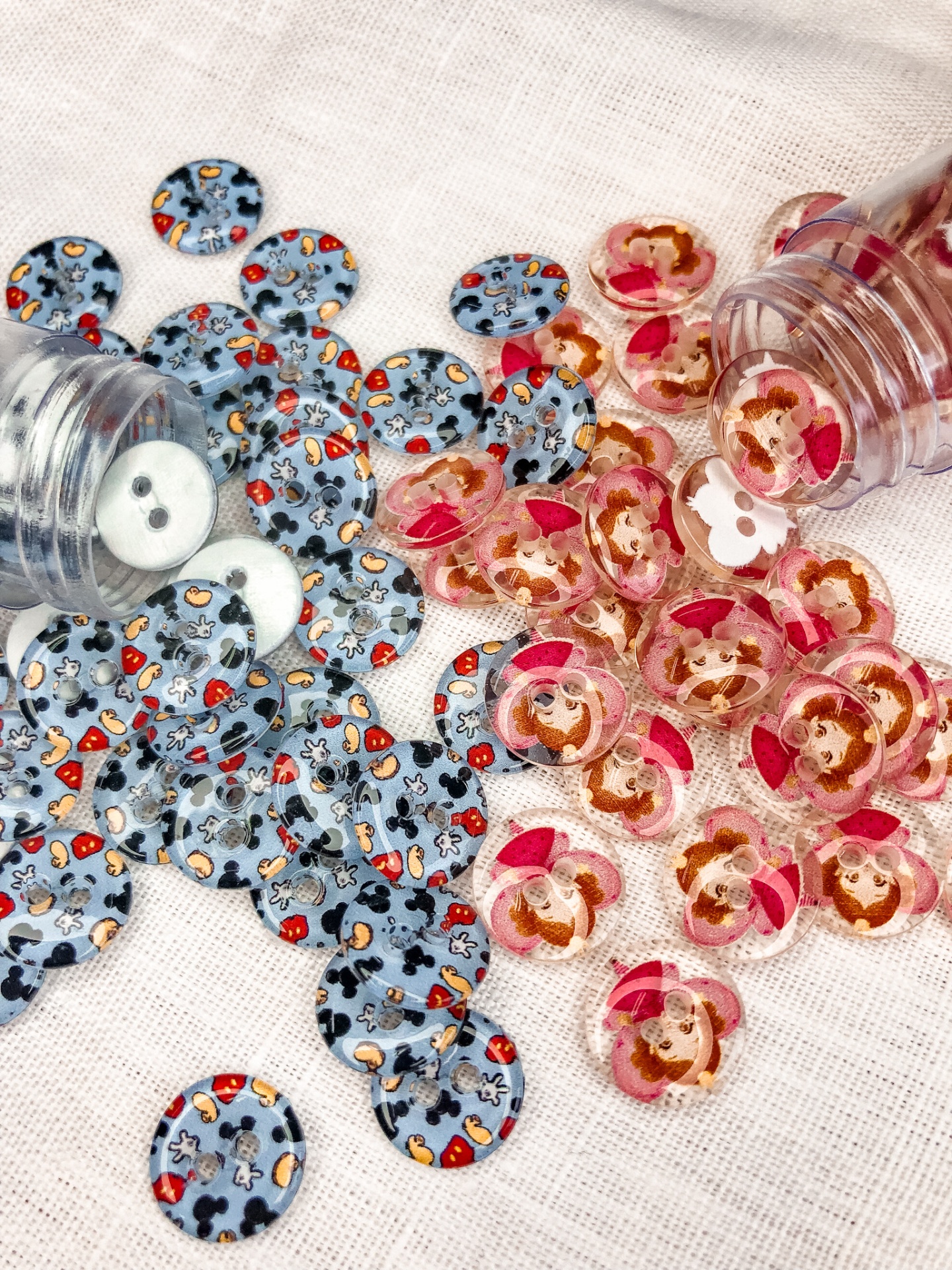 Dois frascos transparentes com botões decorativos azuis e rosa sobre tecido claro