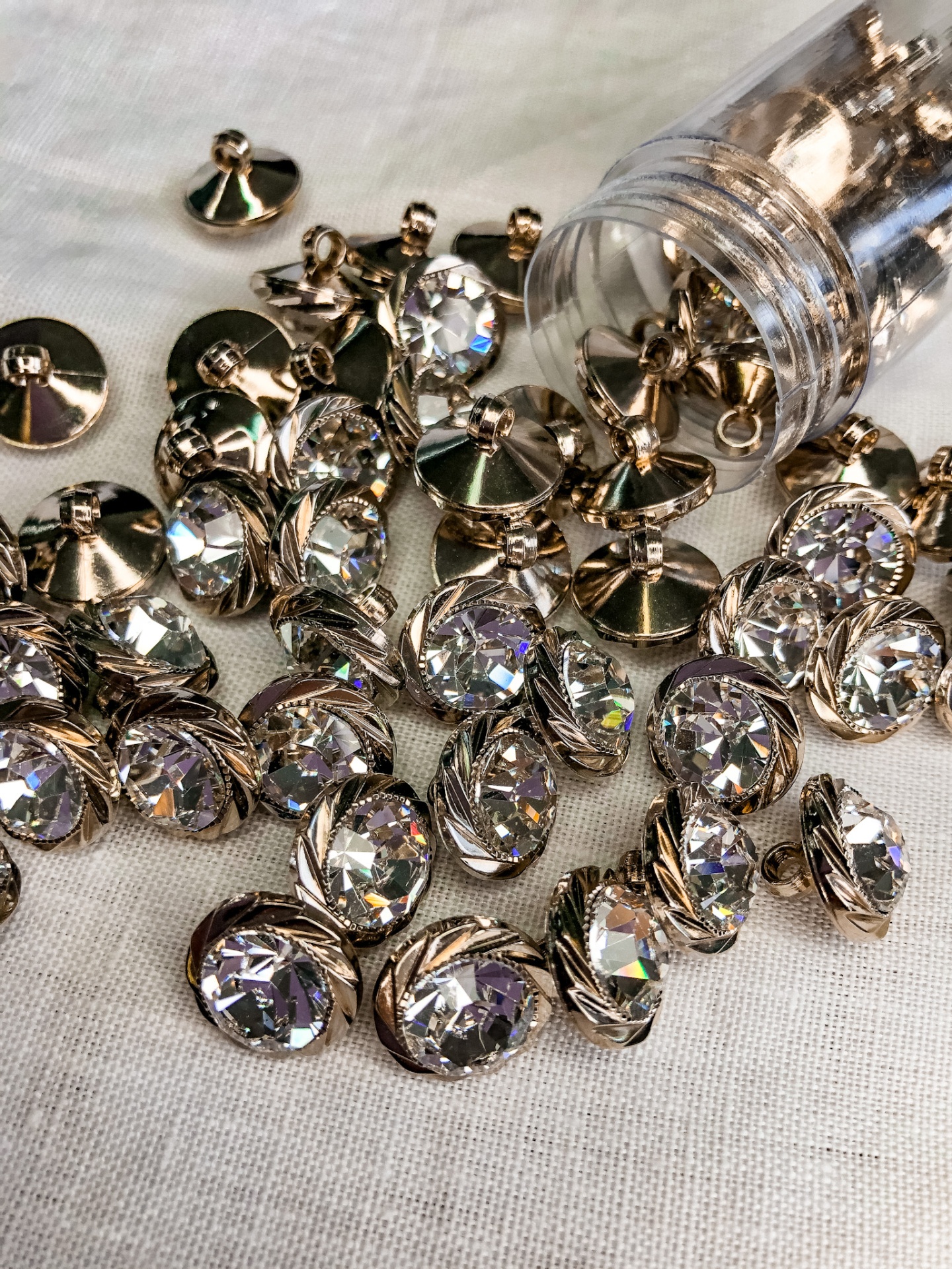 botões redondos dourados com pedra facetada clara sobre tecido branco