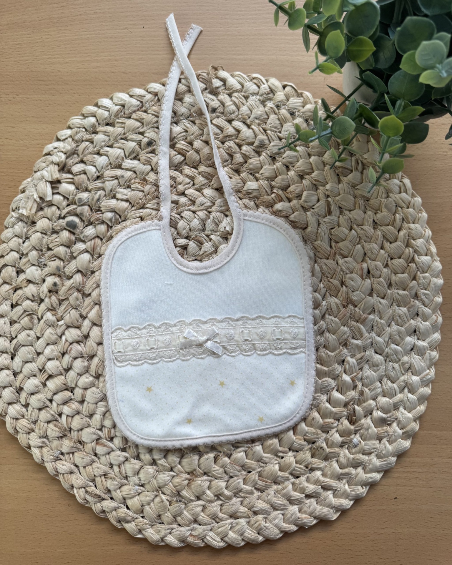 Babete branco decorado sobre tapete de fibras naturais com planta verde ao lado