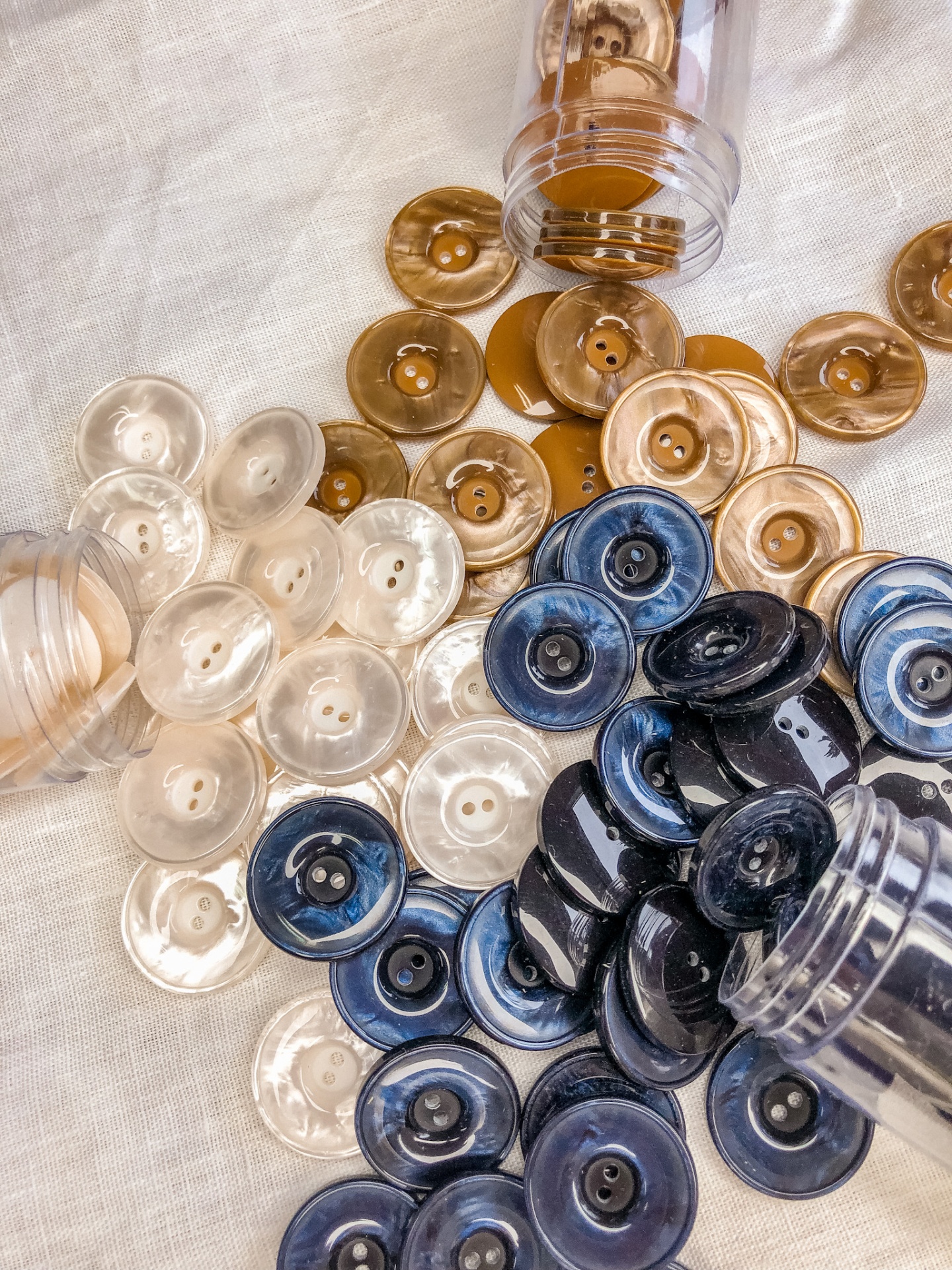 Botões redondos de plástico em castanho, azul marmoreado e bege sobre tecido branco