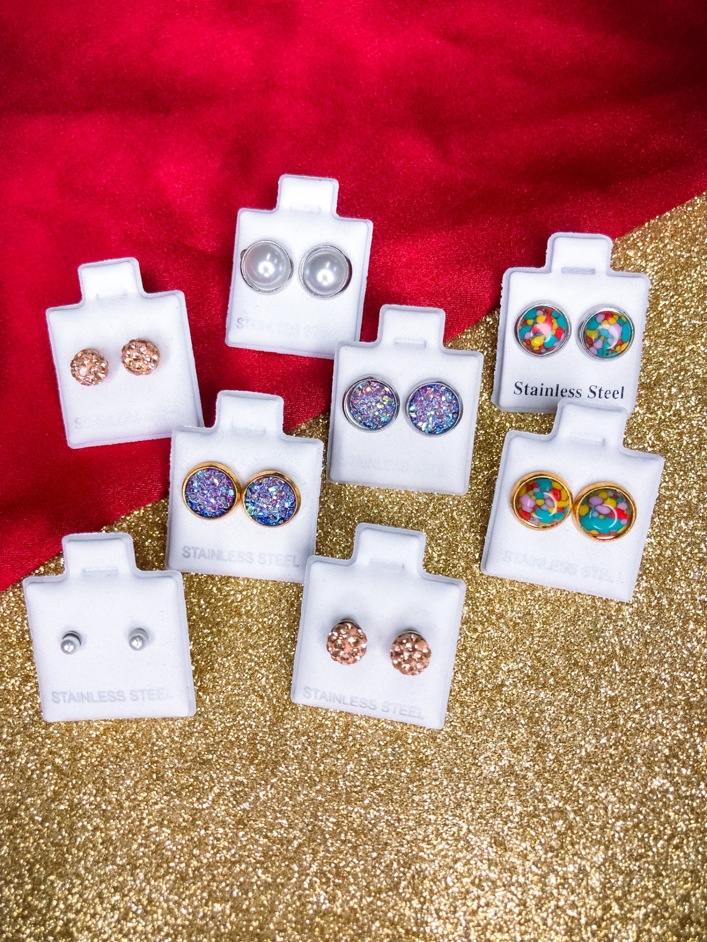 Brincos coloridos em aço inoxidável em suportes de cartão branco sobre fundo vermelho e dourado