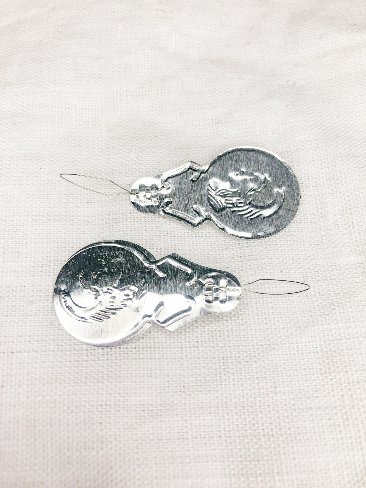 Dois bonecos de neve de metal prateados com fios para pendurar sobre tecido branco