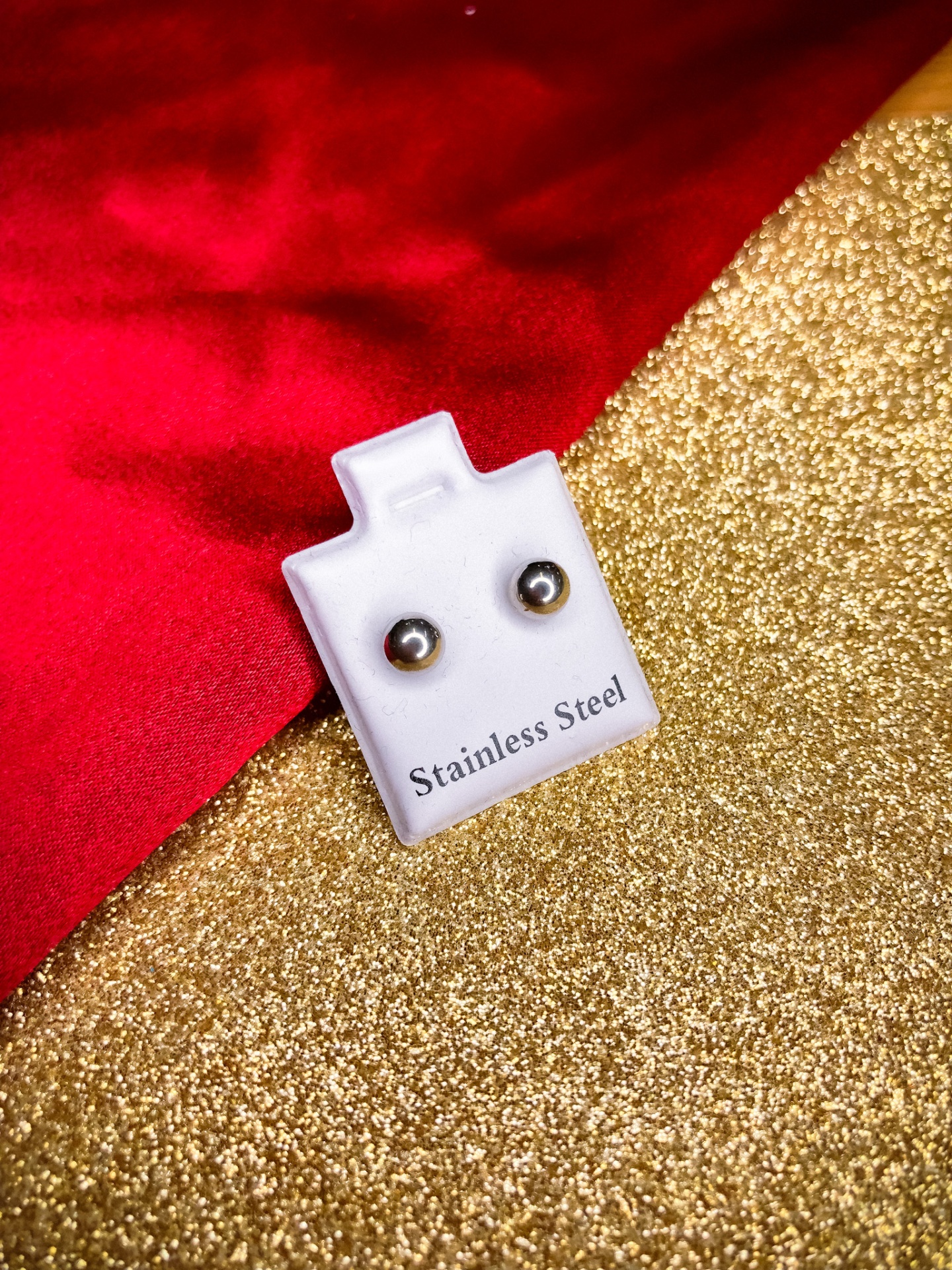 Brincos de aço inoxidável em suporte branco sobre fundo dourado e vermelho