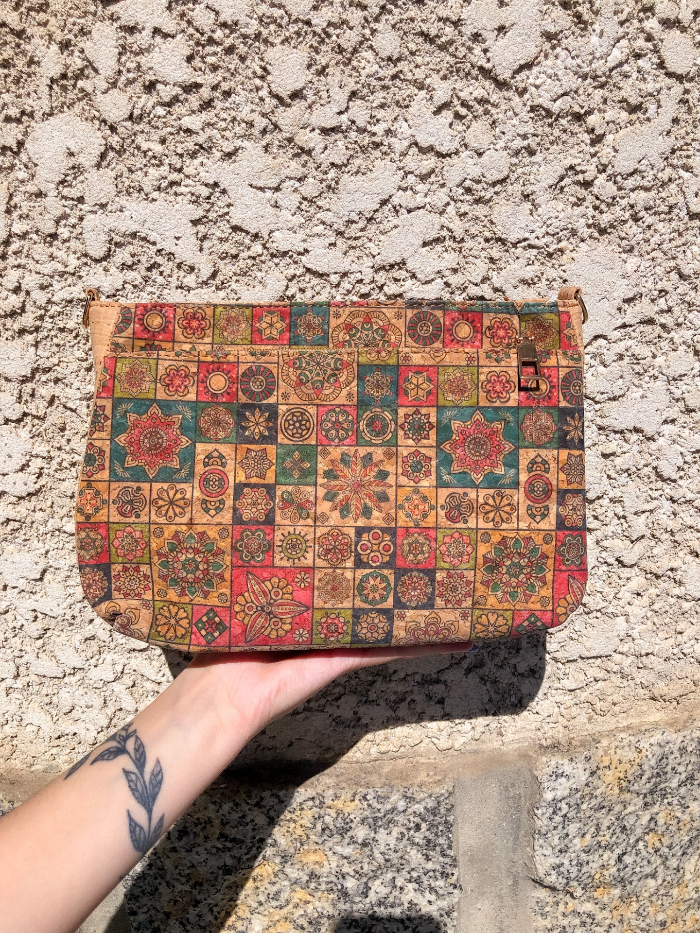 Bolsa de mão com padrão geométrico e floral multicolor e mão tatuda segurando