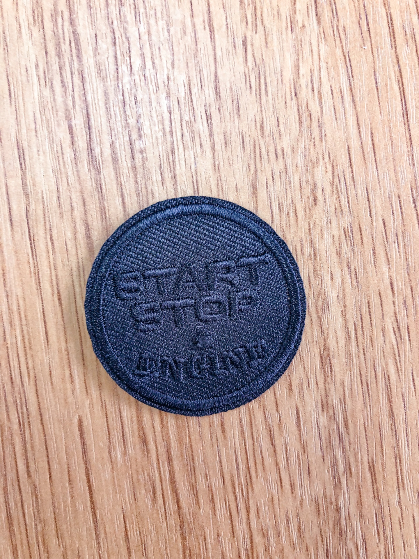 Emblema redondo em tecido preto com texto Start Stop Engine sobre madeira