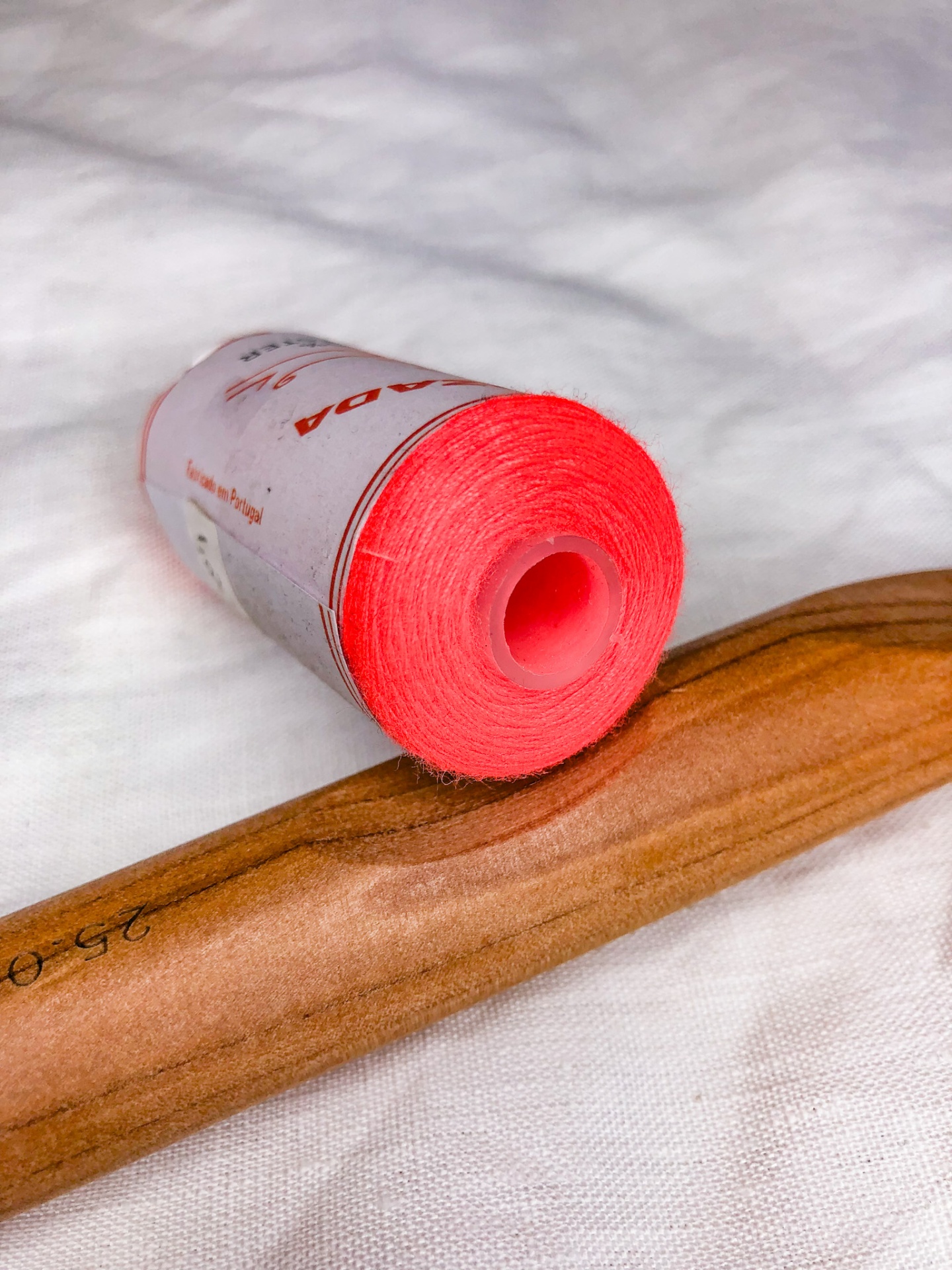 Rolo de linha vermelho vivo com carretel plástico e objeto de madeira polida sobre tecido branco