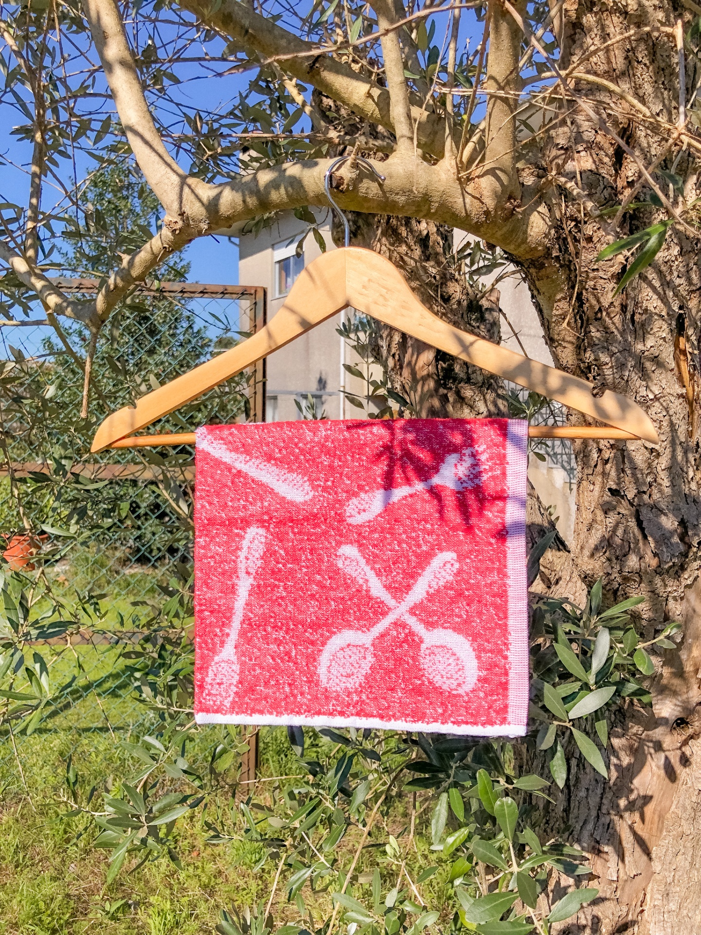 Toalha vermelha com padrão de colheres branca pendurada em cabide de madeira numa árvore