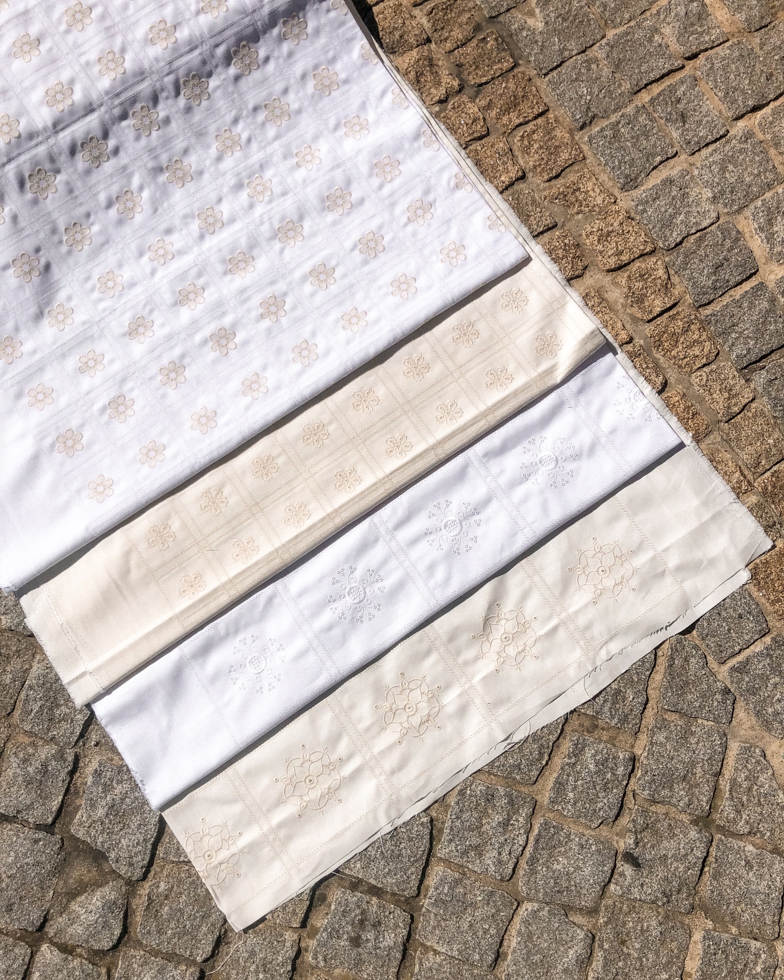 Quatro tecidos bordados em branco e bege sobre calçada de pedra