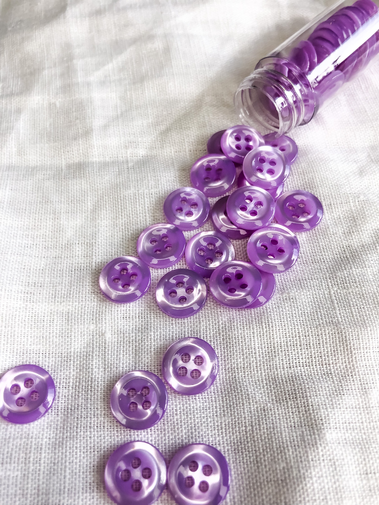Botões roxos translúcidos espalhados sobre tecido branco, alguns dentro de frasco transparente