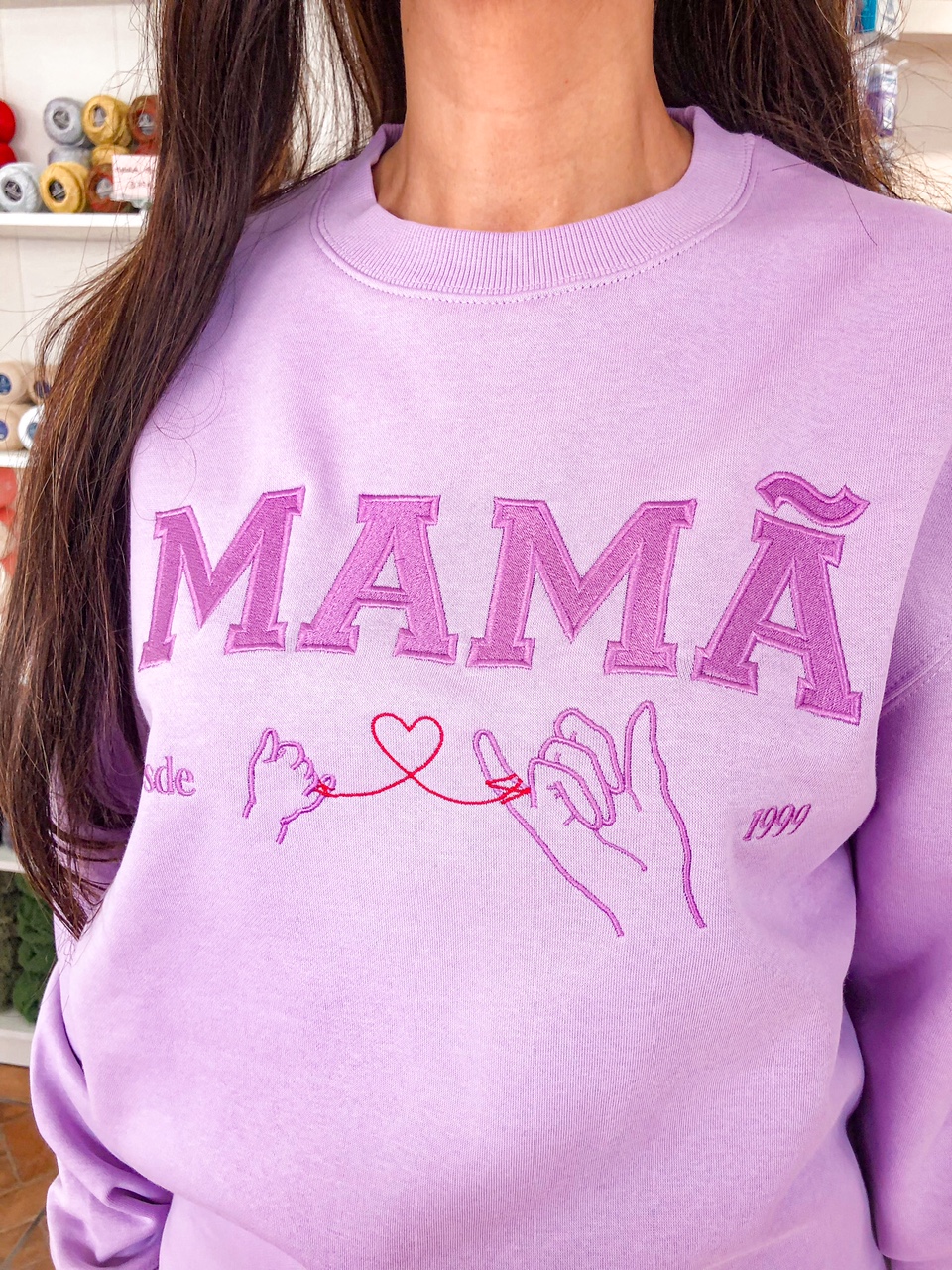 Sweatshirt lilás bordada com palavra MAMÃ e desenho de mãos unidas por fio vermelho em forma de coração.