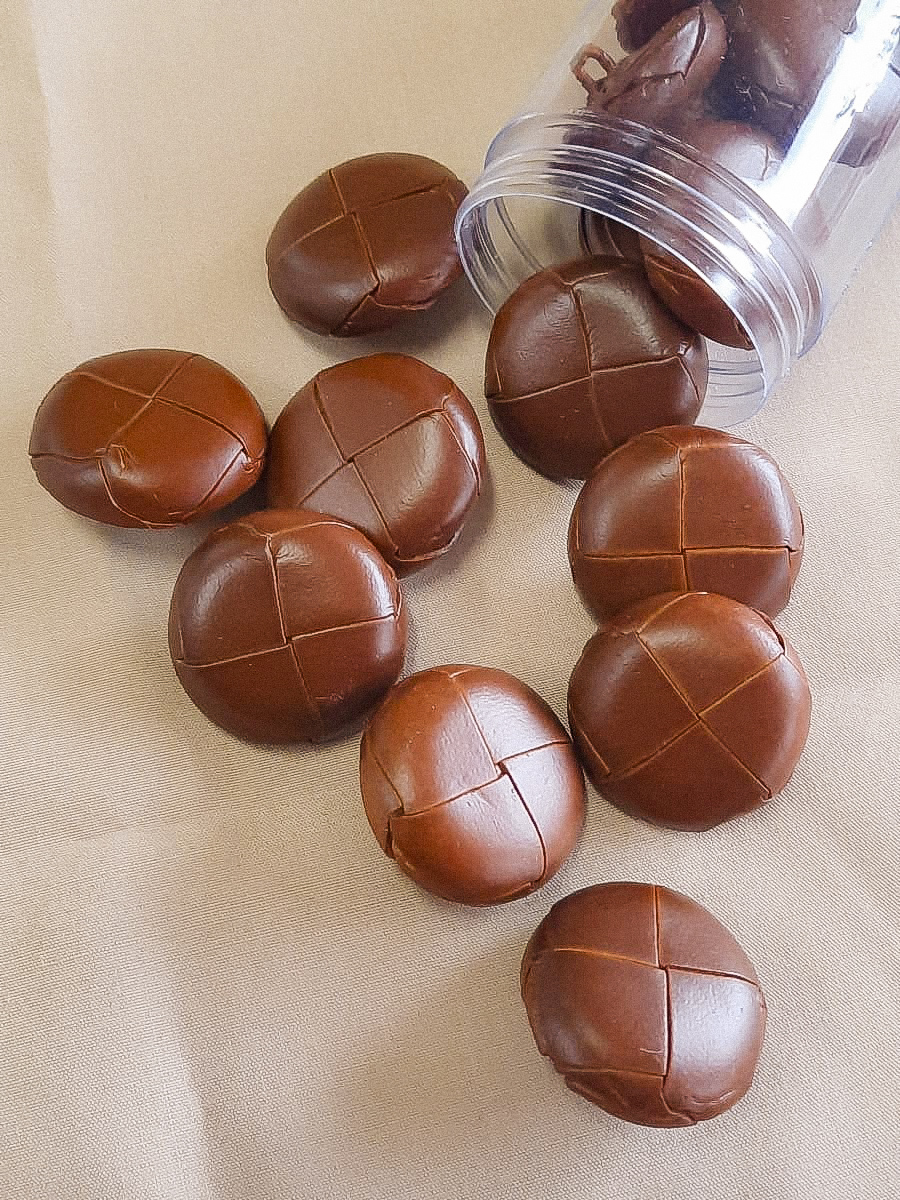 botões castanhos redondos com padrão cruzado em recipiente plástico e superfície bege