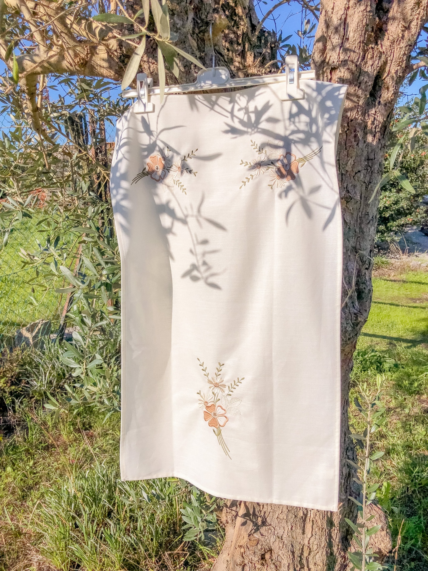 Pano branco bordado pendurado num ramo de árvore em ambiente exterior