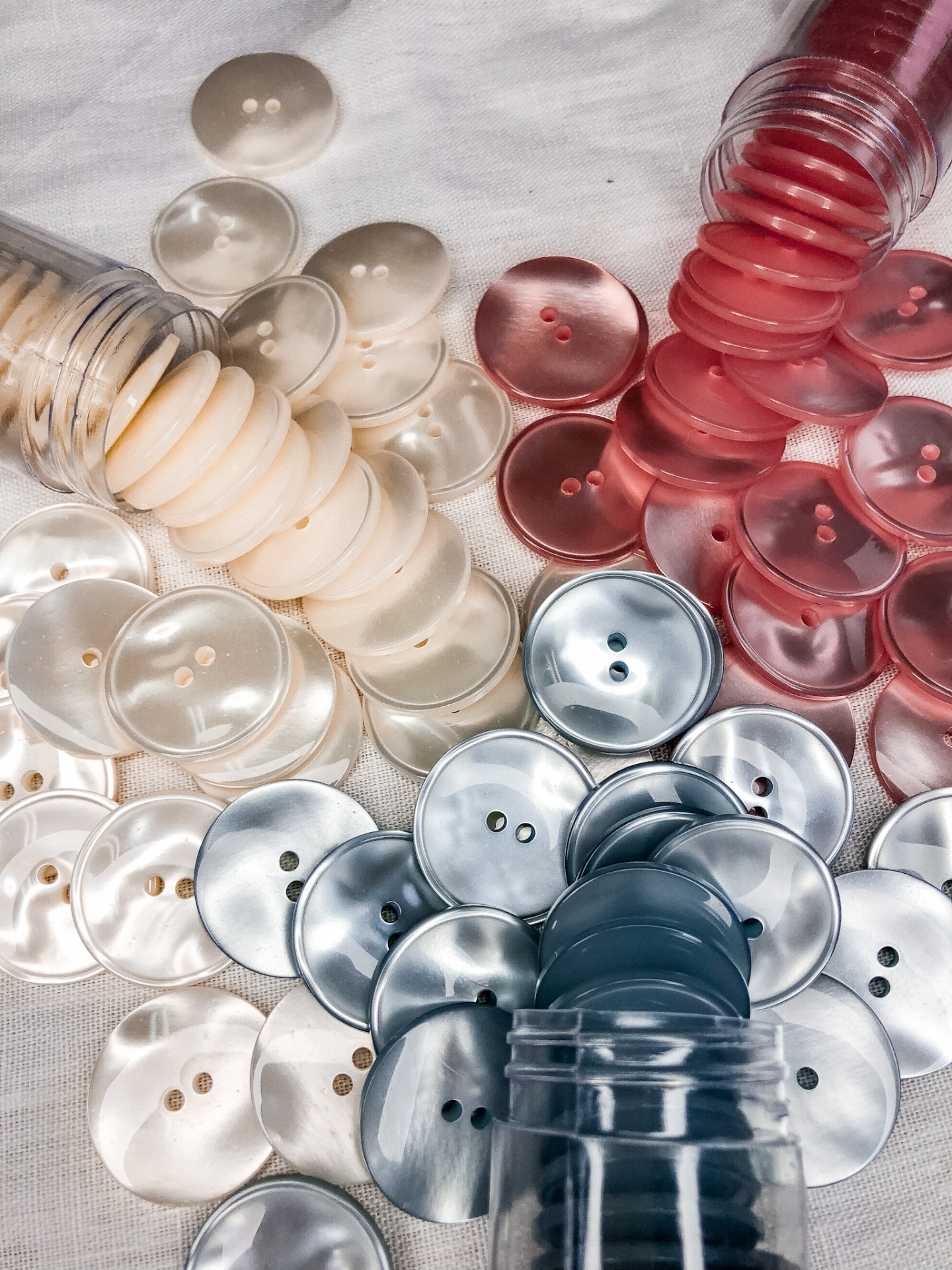 Botões redondos coloridos em plástico sobre tecido branco, com vários frascos transparentes