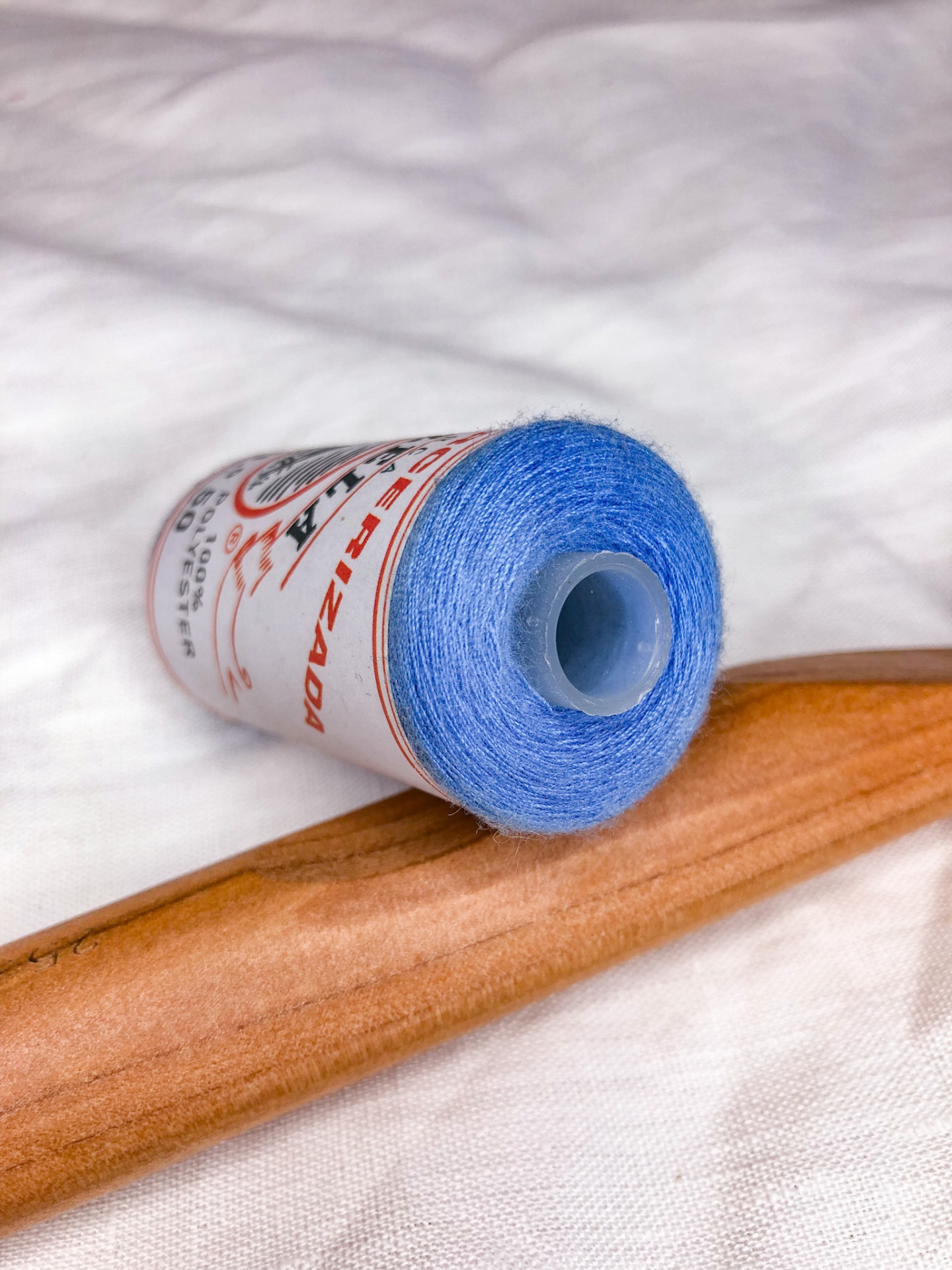 Carretel de linha azul com rótulo com texto, sobre tecido branco e madeira