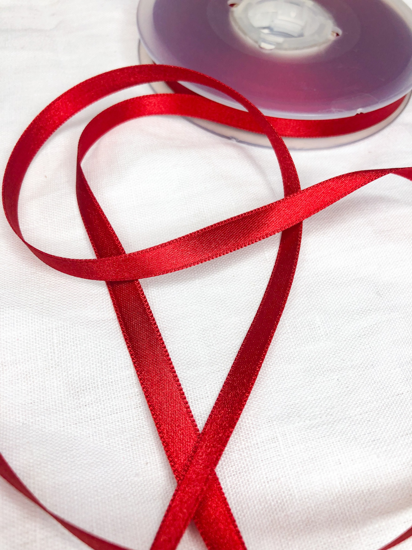 Fita vermelha de cetim fina num carretel plástico transparente