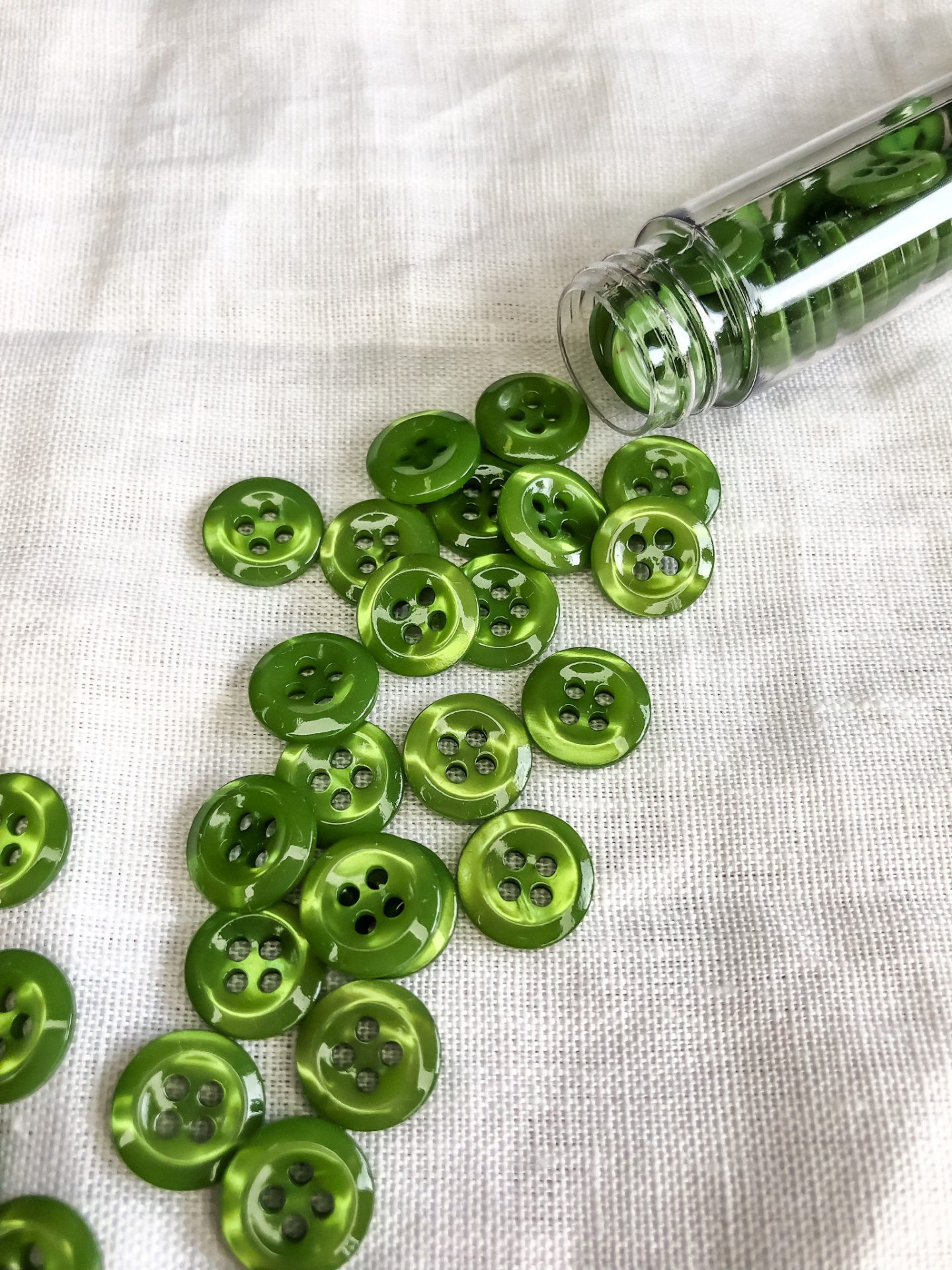 Botões verdes de plástico com quatro furos espelhados sobre tecido branco ao lado de um tubo transparente aberto