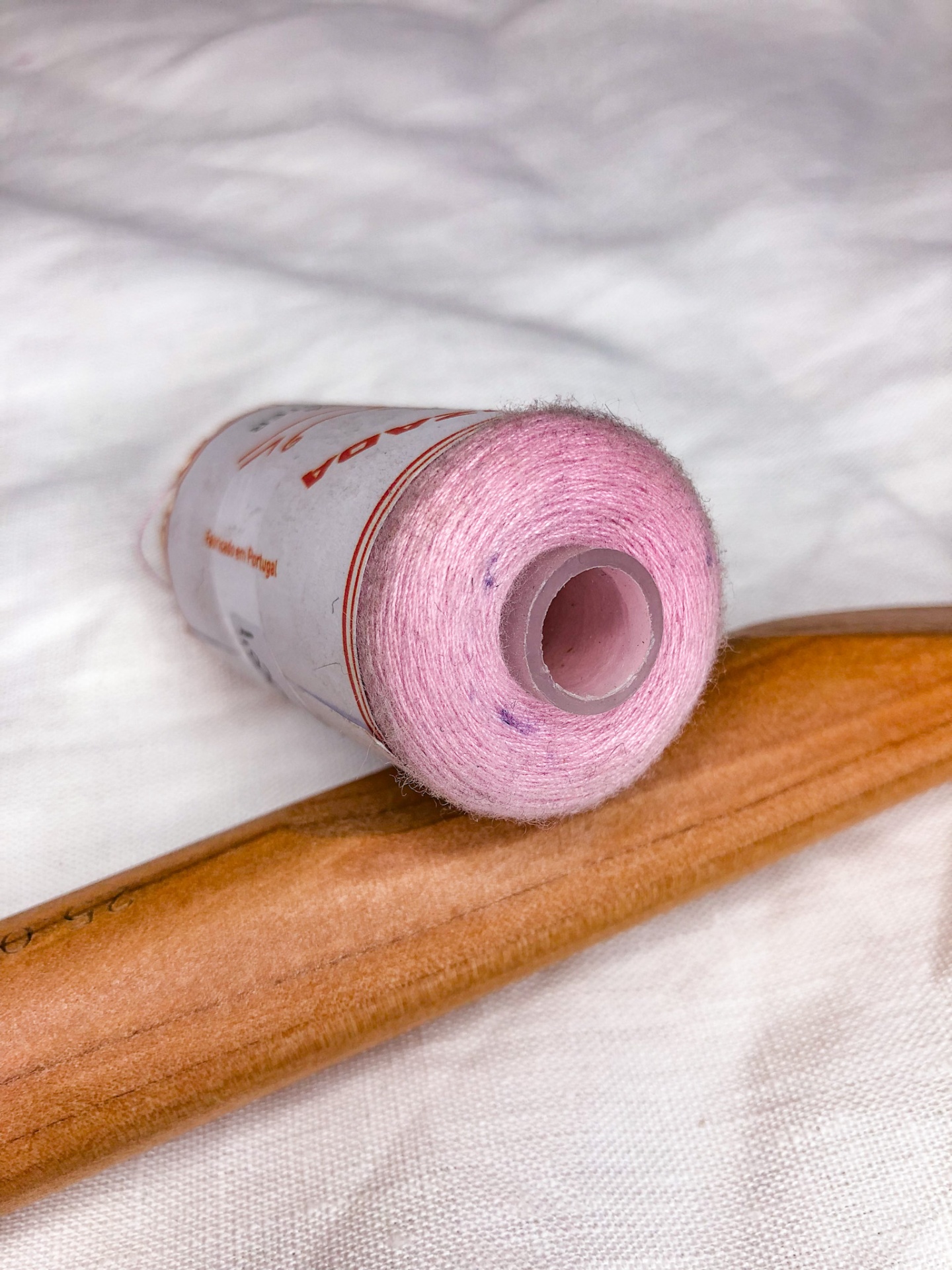 Carretel de linha cor-de-rosa sobre objeto de madeira clara em tecido branco