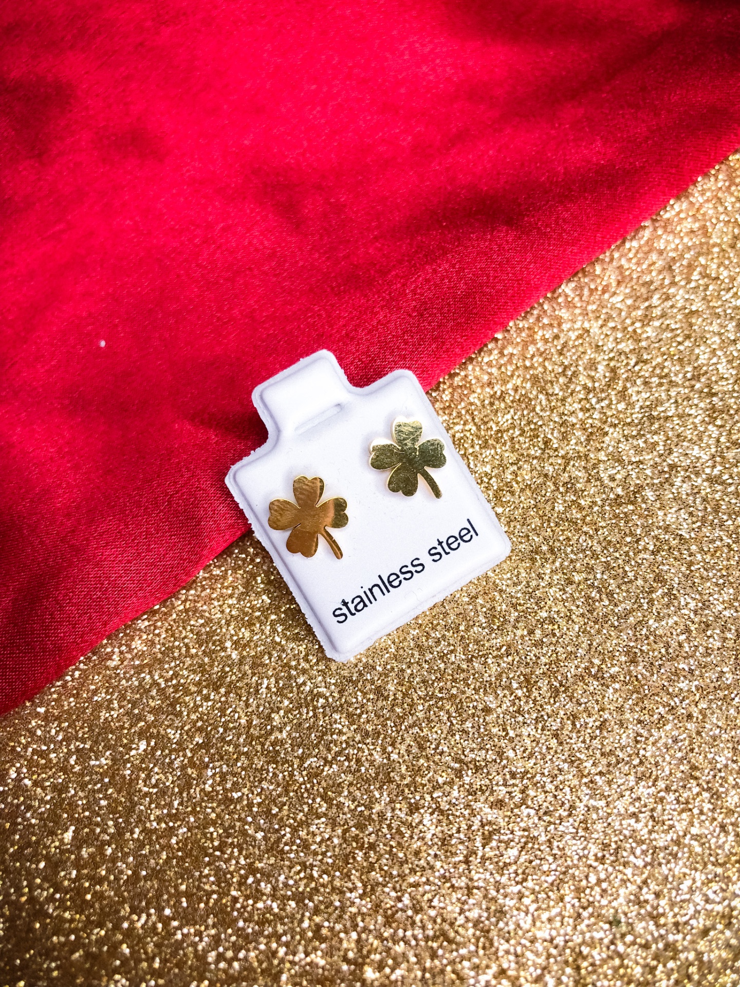 Brincos de aço inox dourados em forma de trevo de quatro folhas num suporte branco