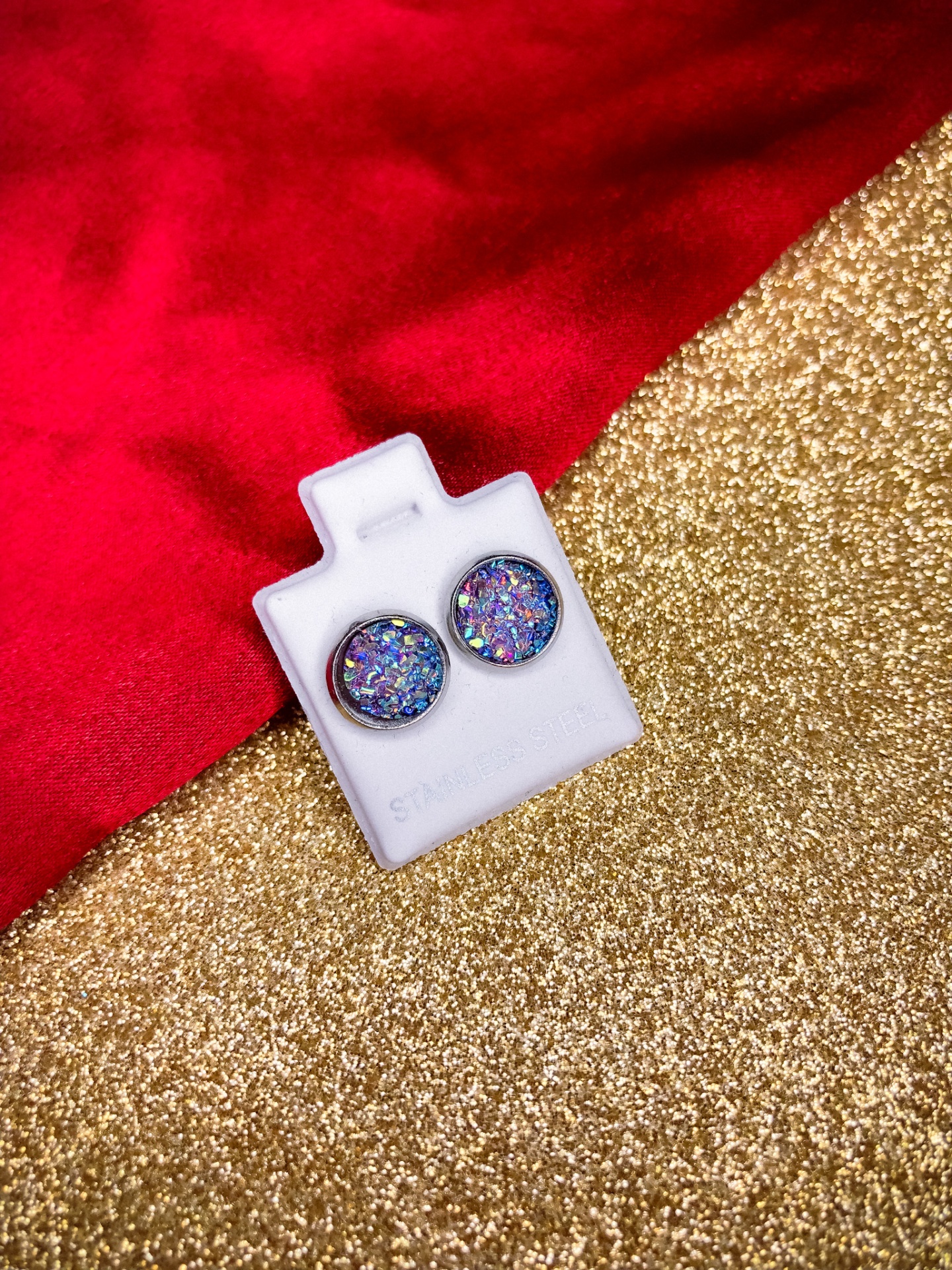 Brincos redondos brilhantes em suporte branco sobre fundo dourado e vermelho