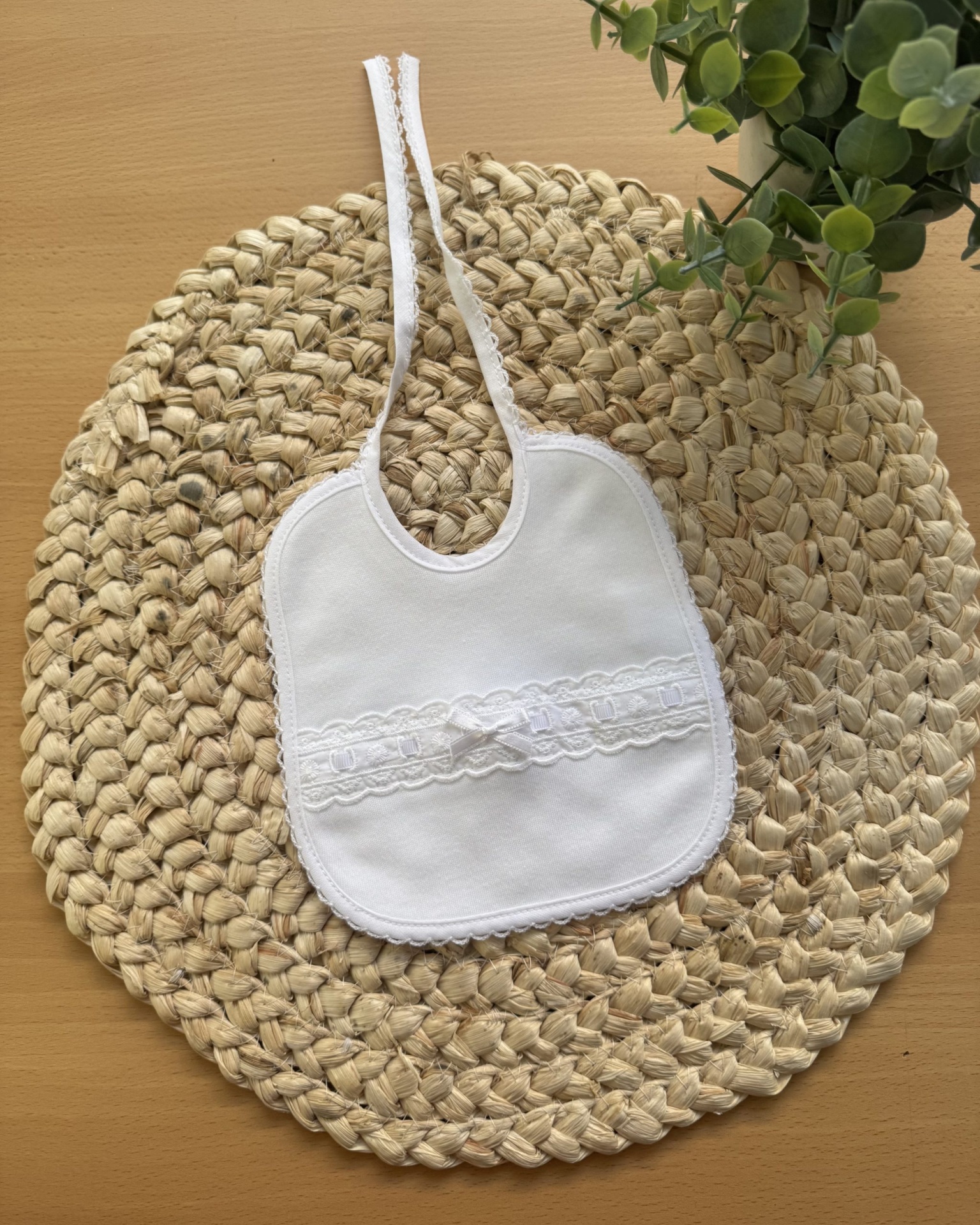 Babete branco com renda e laço sobre base de palha clara