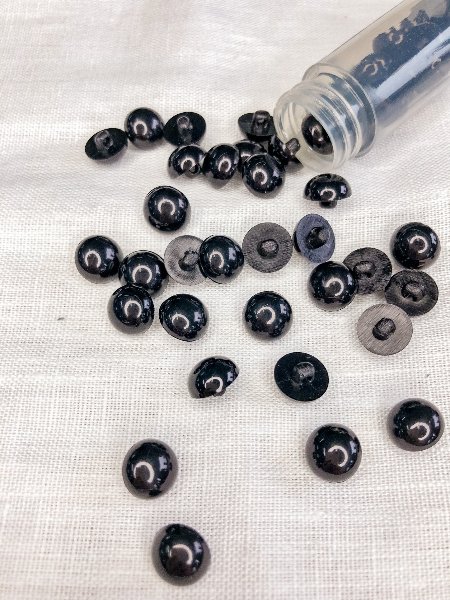 botões de pressão metálicos pretos brilhantes e foscos espalhados em tecido bege com tubo plástico