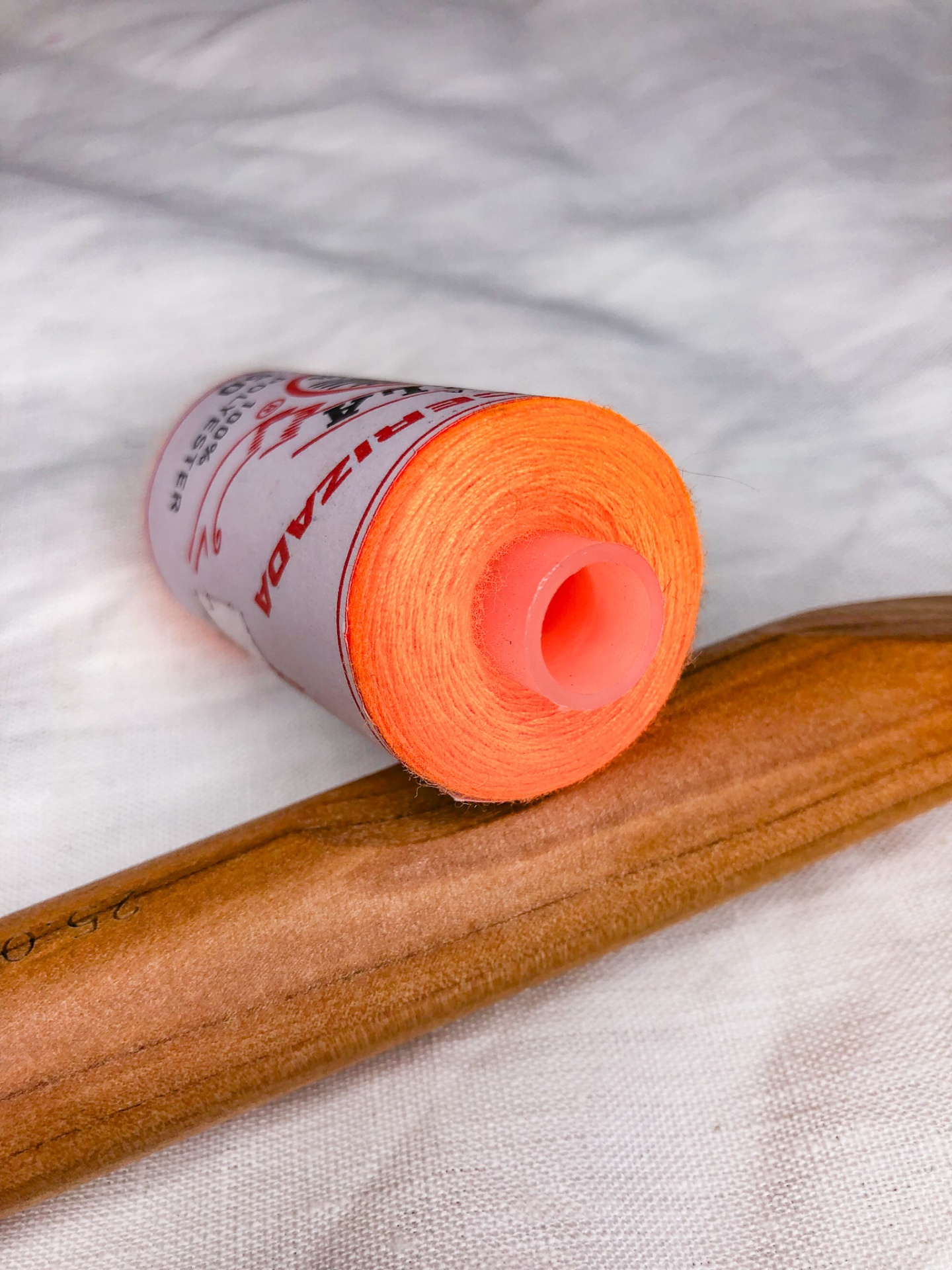 Rolo de linha laranja com bobina de plástico sobre tecido branco e objeto de madeira