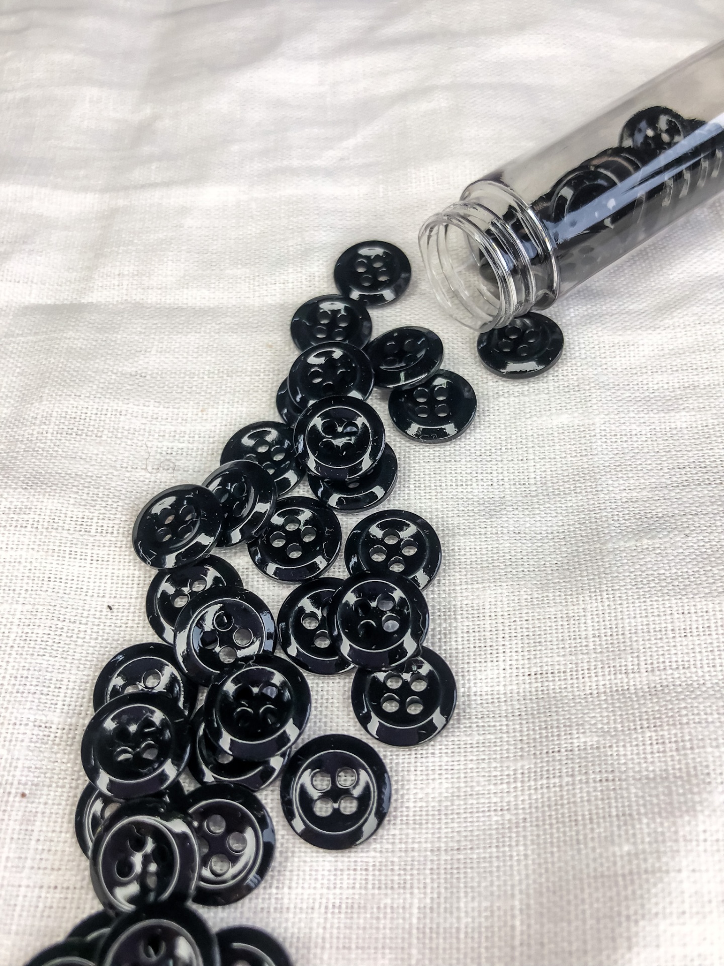 Botões pretos de quatro furos espalhados sobre tecido branco