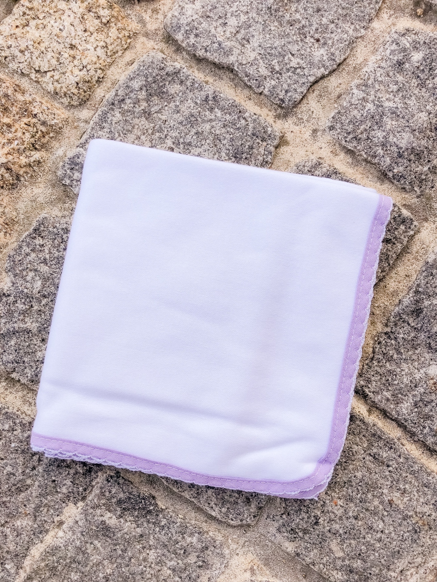 Lenço branco com borda lilás sobre chão de pedra cinza