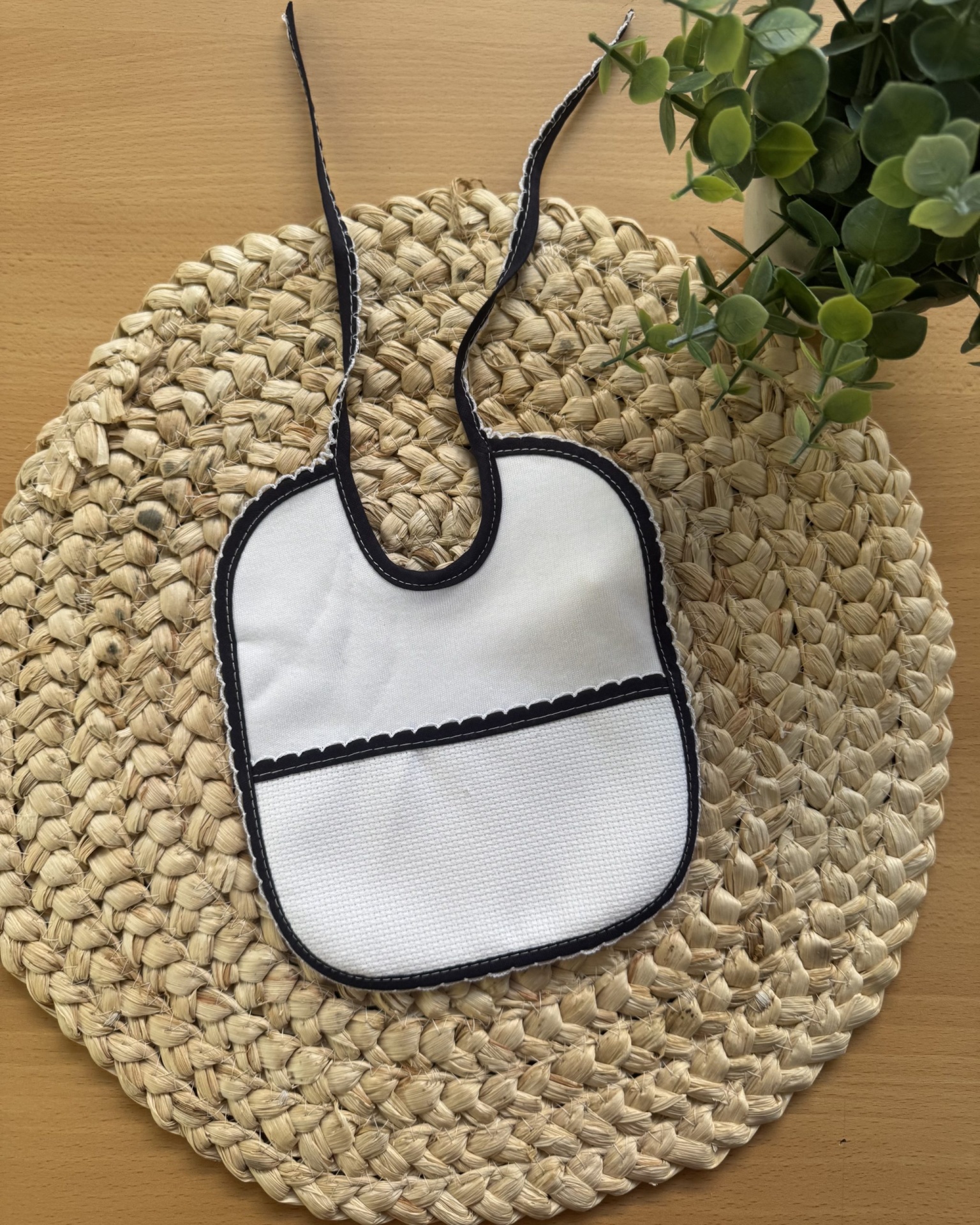 Babete branco com borda preta sobre base de fibra natural e planta verde