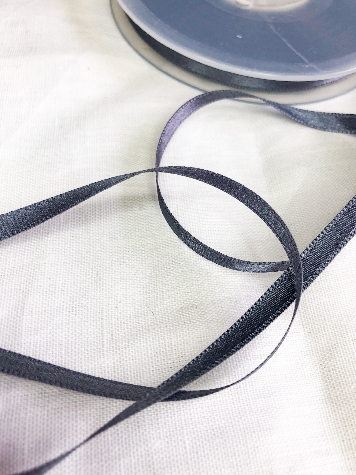 Fita de cetim preta fina desenrolada com bobina cinza