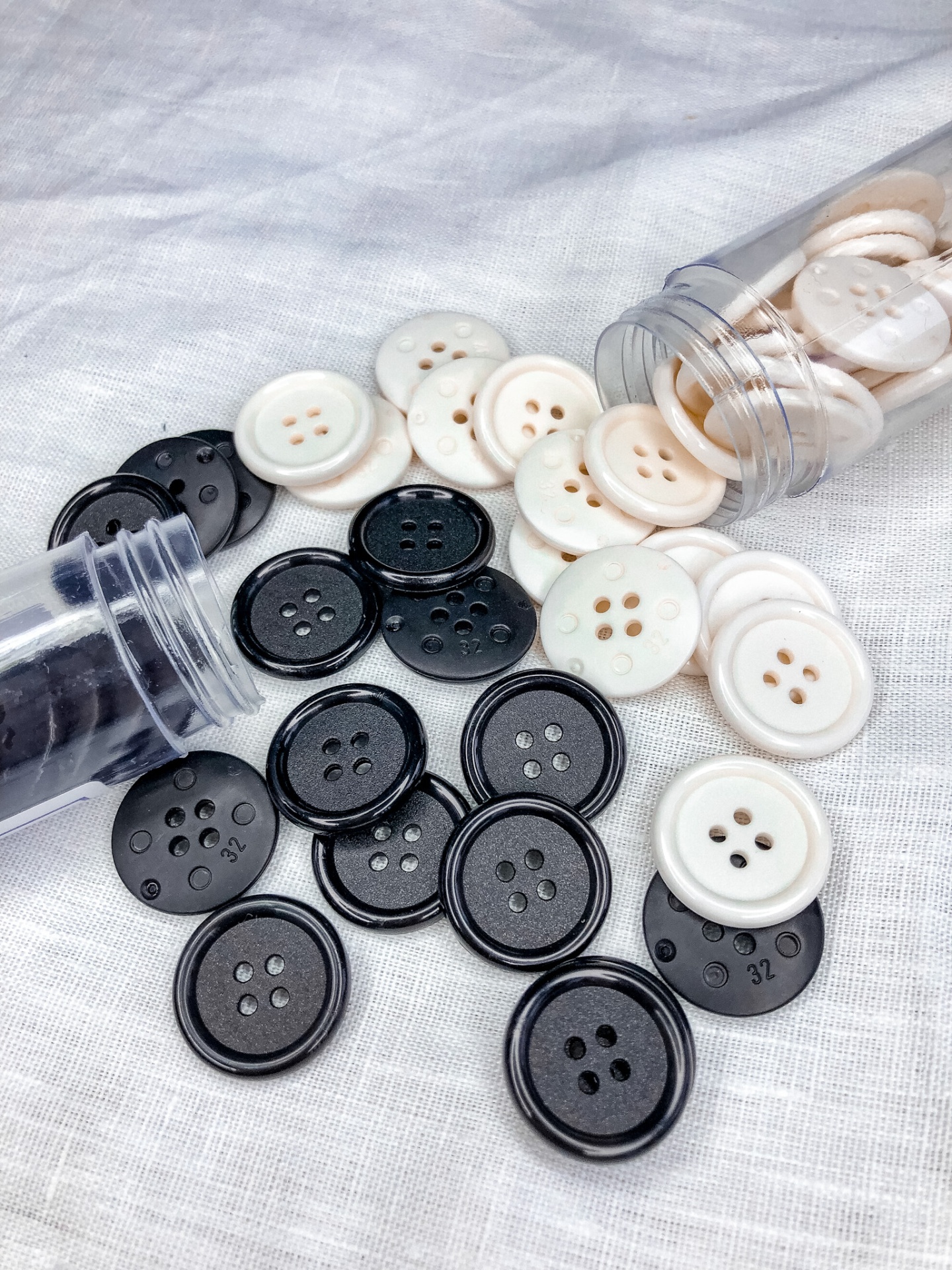 Botões redondos brancos e pretos com quatro furos em tecido branco.