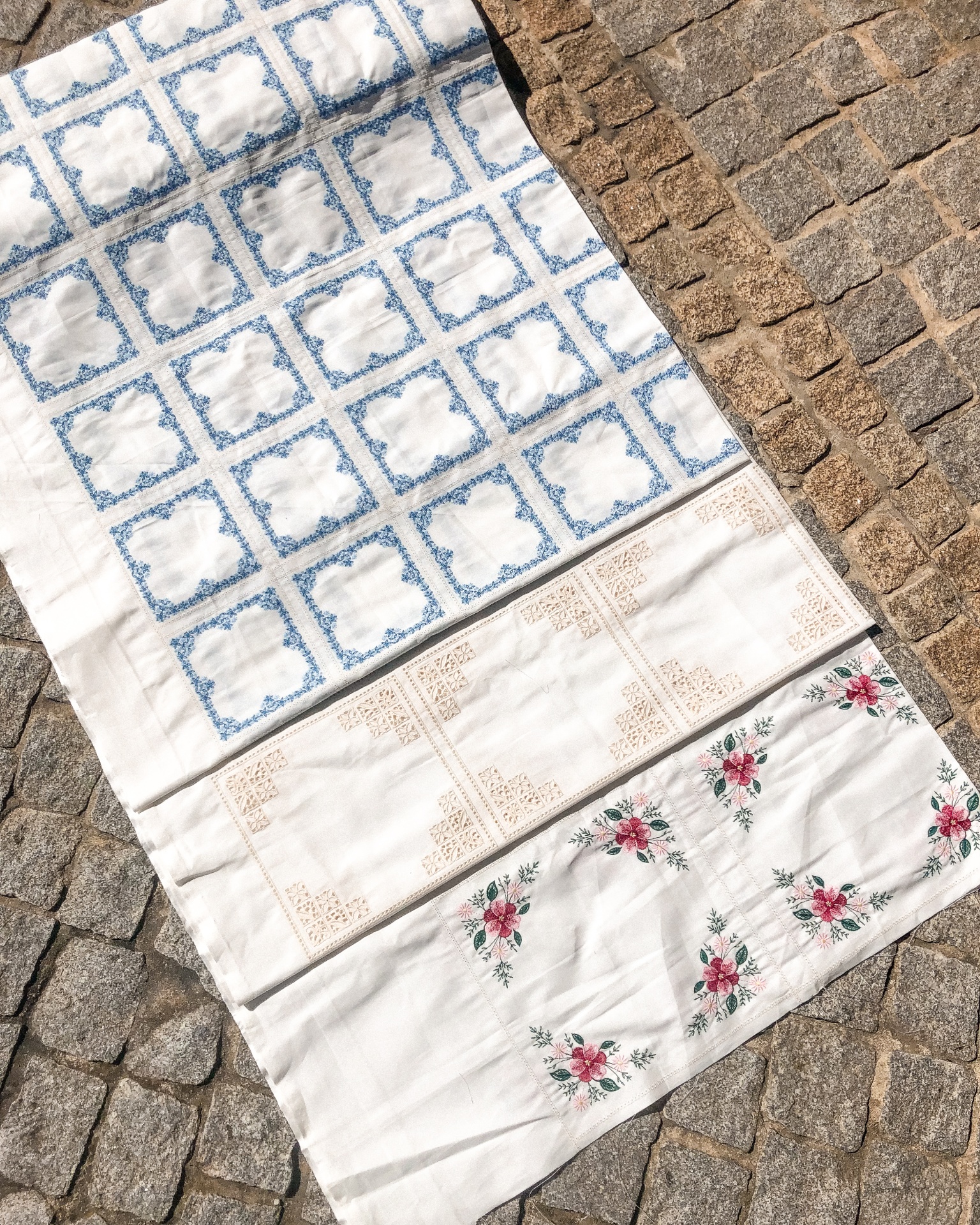 Três panos de tecido com padrões azul, castanho e floral sobre calçada de pedras