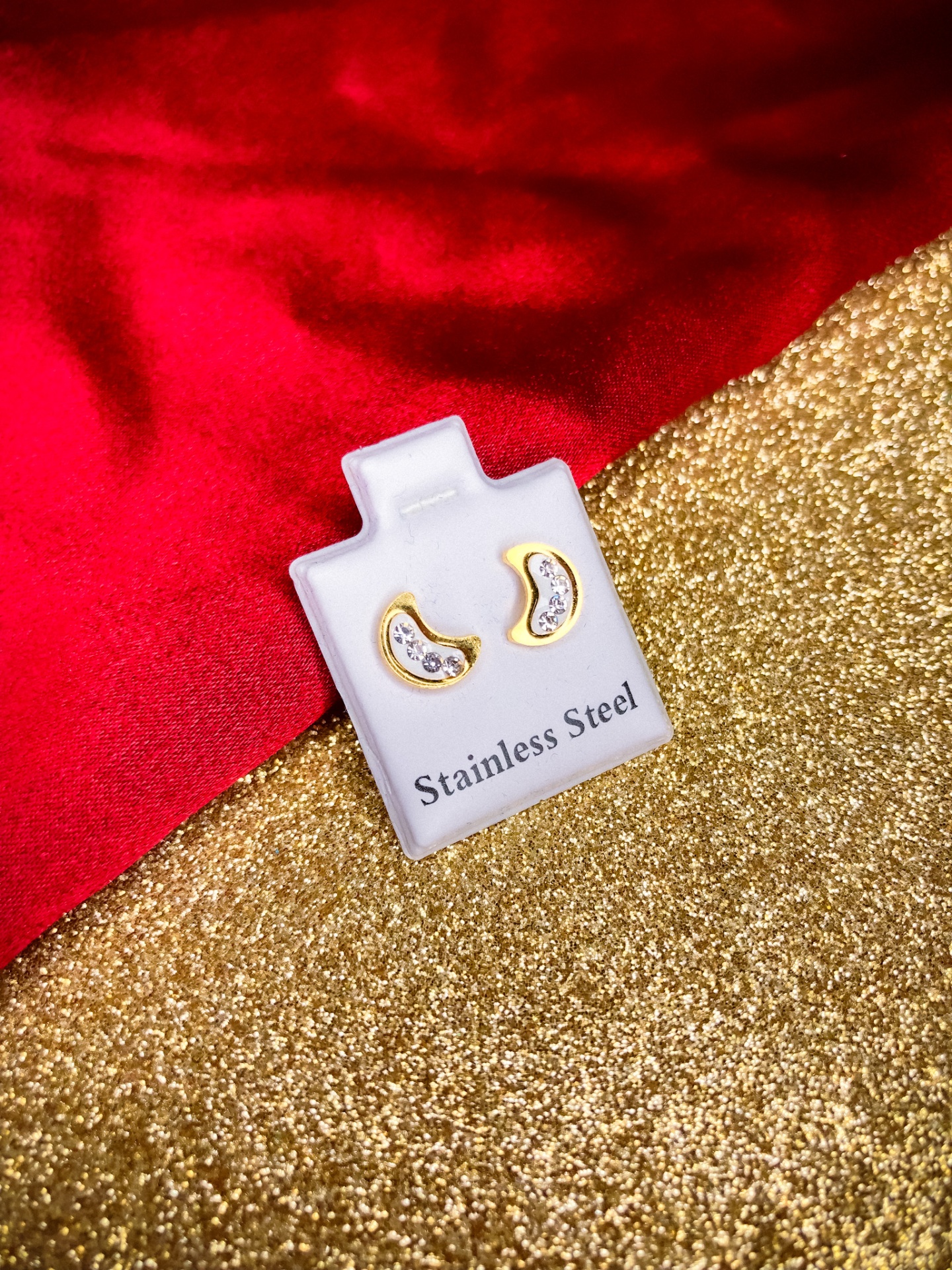 Brincos em aço inoxidável em cartão branco com fundo vermelho e dourado