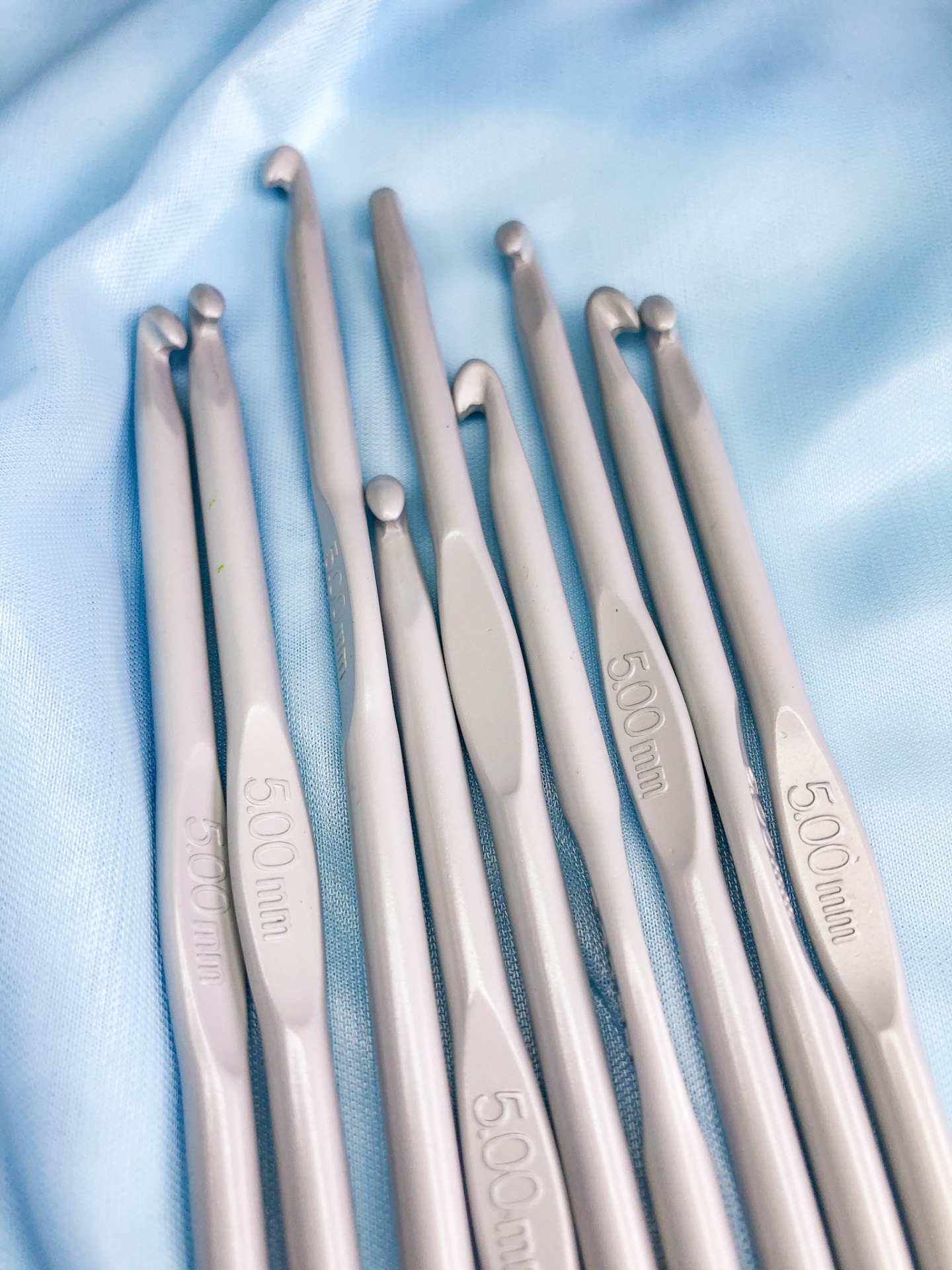 Agulhas de crochet metálicas prateadas com medida 5.00 mm sobre tecido azul claro