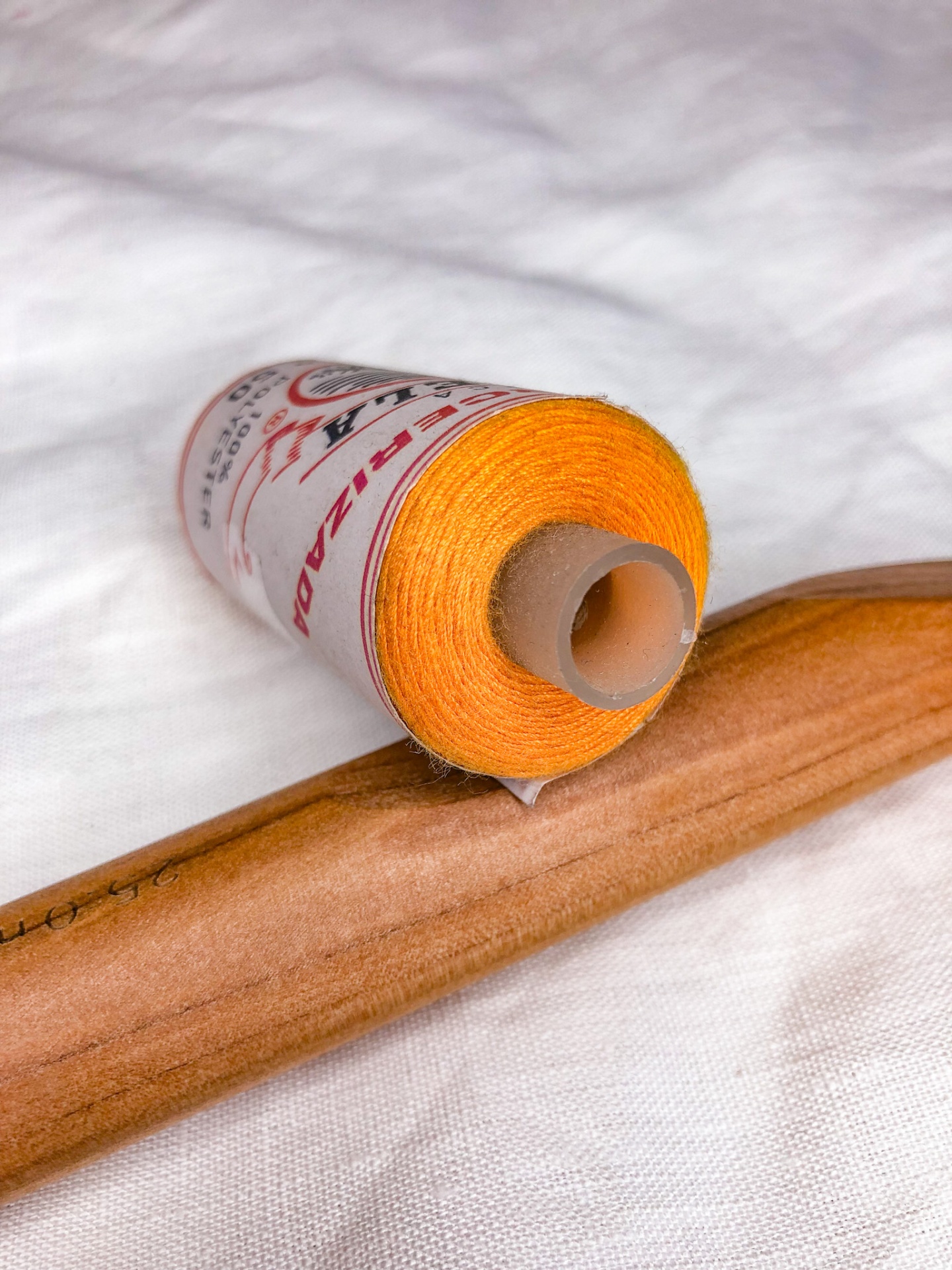 carretel de fio amarelo com etiqueta e ferramenta de madeira sobre tecido branco