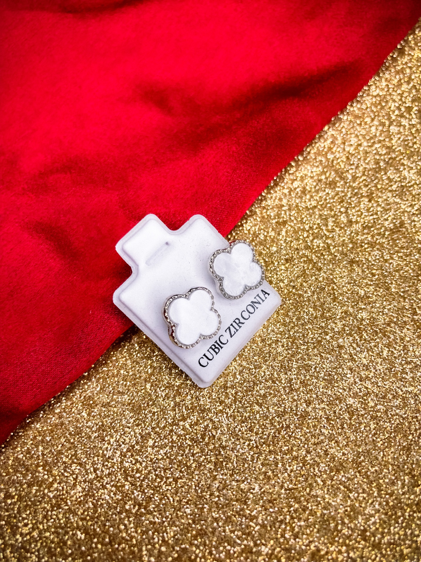 Brincos flor de cubos de zircónio num suporte branco sobre fundo dourado e vermelho.