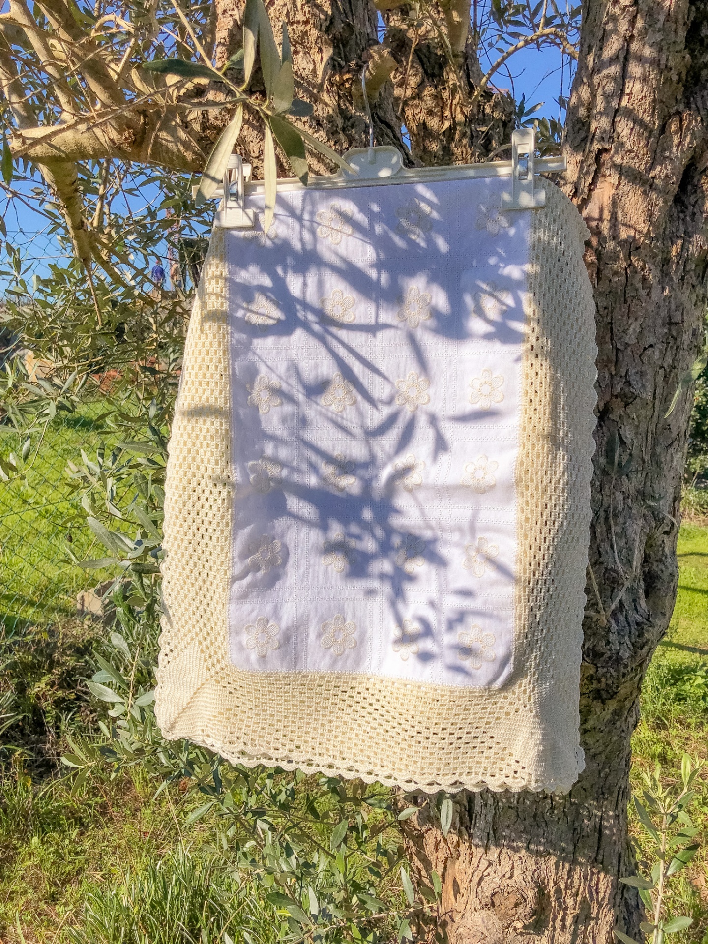 Manta branca com bordado dourado e renda bege pendurada numa árvore