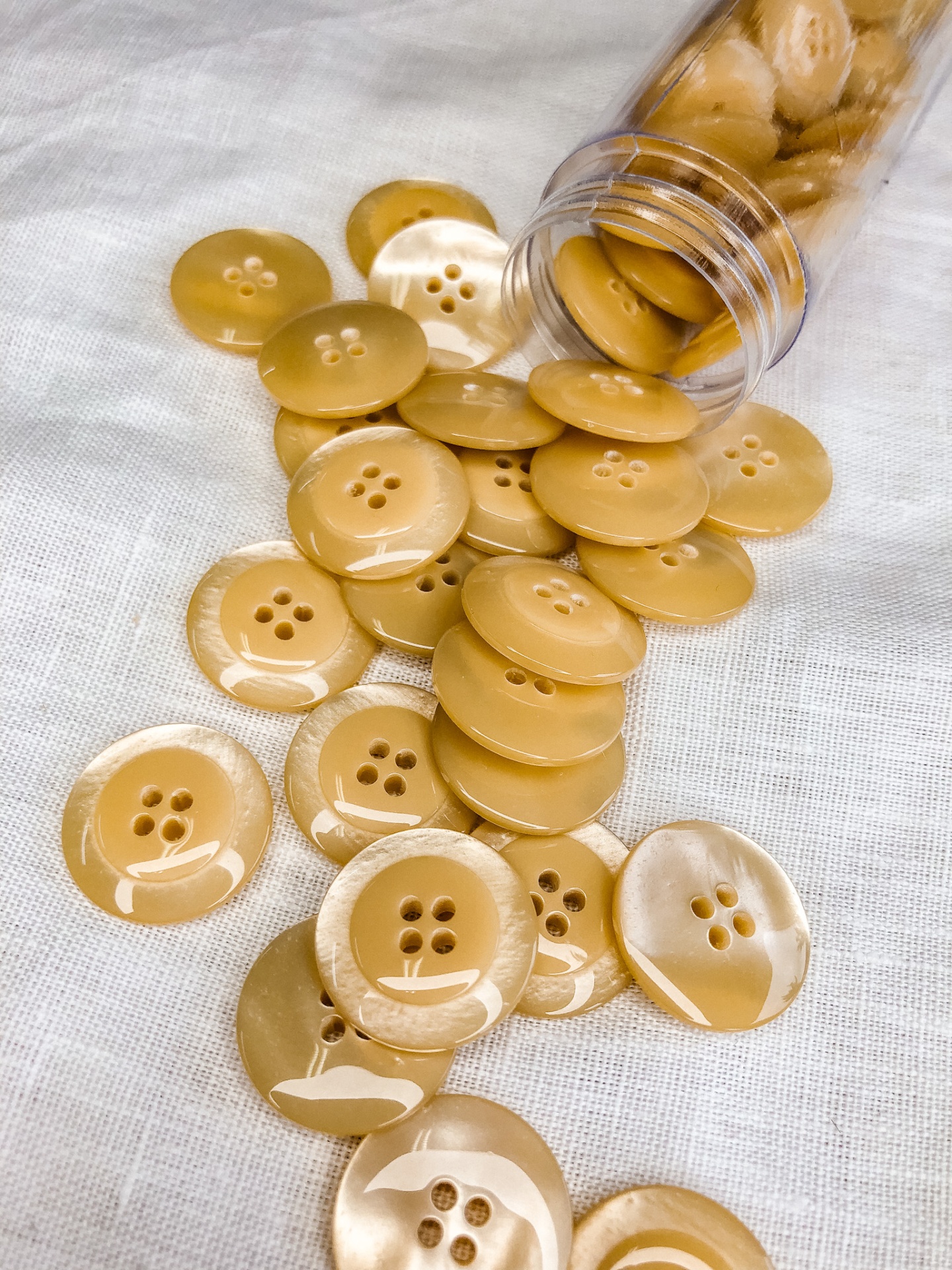 Botões castanhos claros redondos com quatro furos sobre tecido branco e frasco plástico