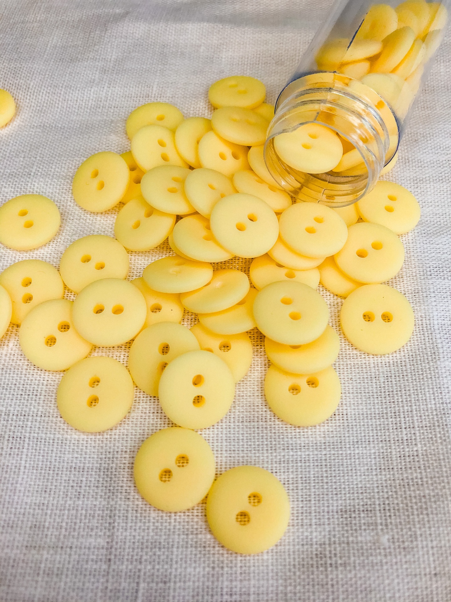 Botões amarelos de plástico espalhados com frasco aberto sobre tecido claro