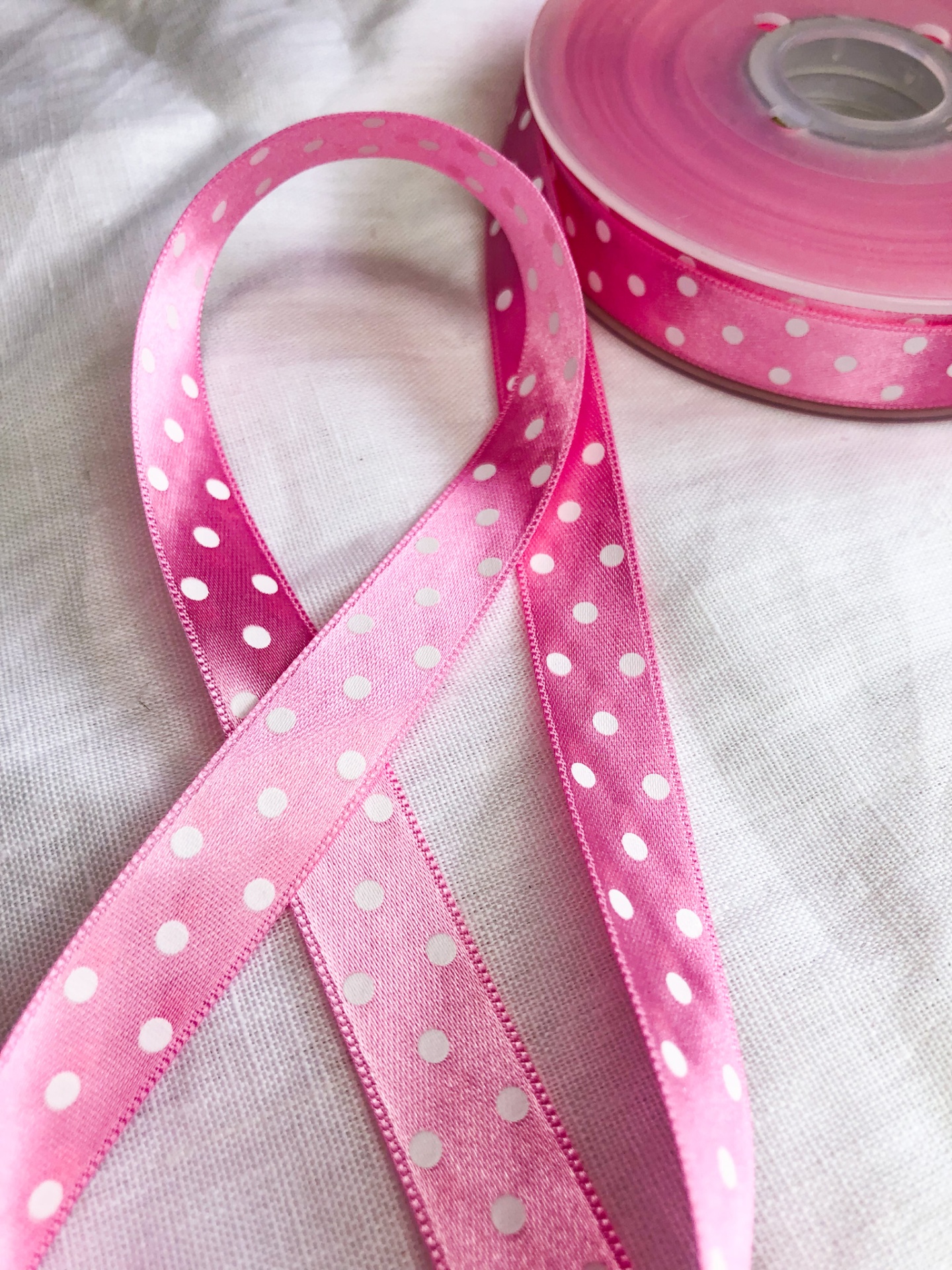 Fita de cetim cor-de-rosa com bolinhas brancas desenrolada sobre tecido branco