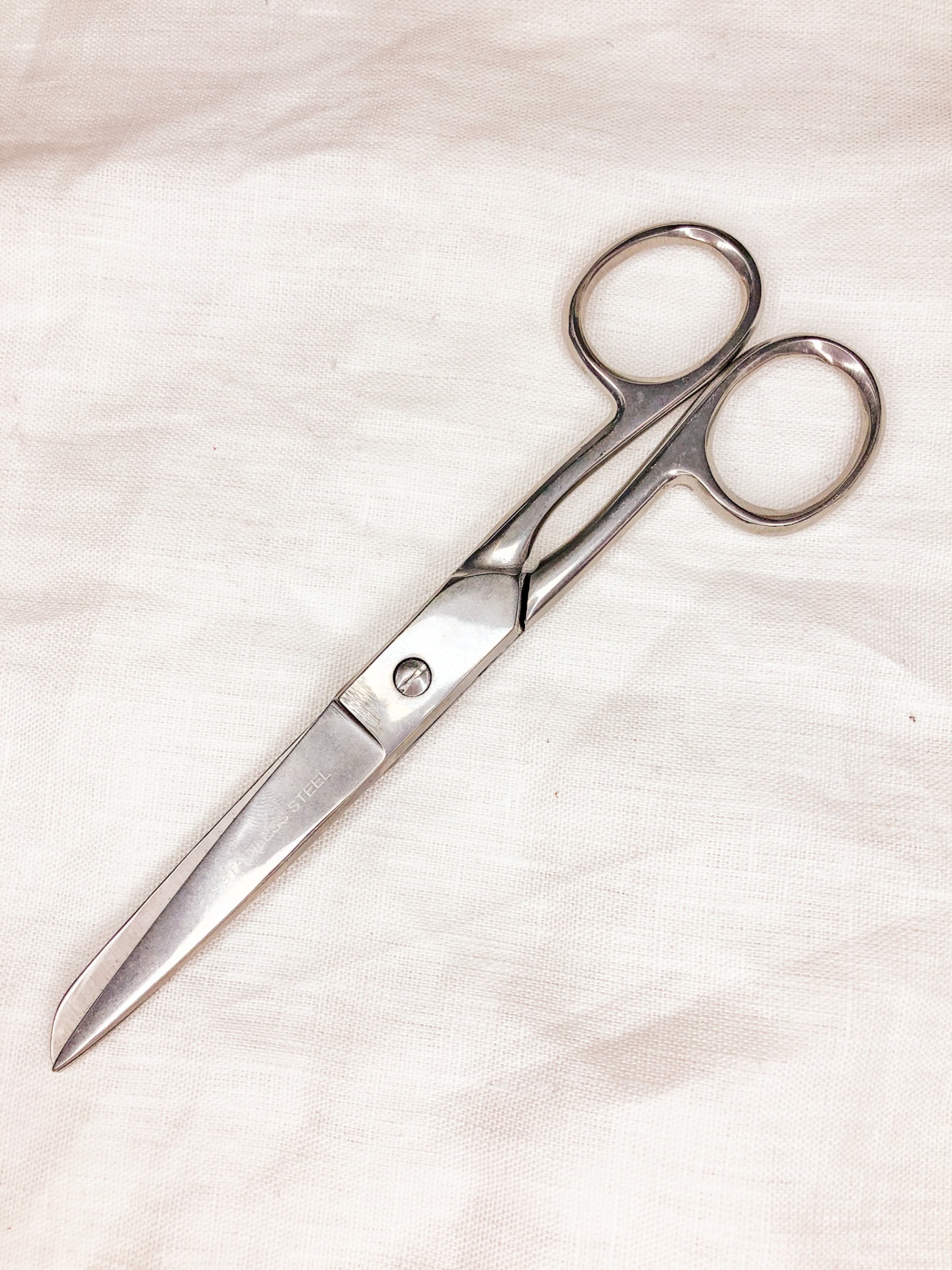 Tesoura metálica com cabo em argola sobre tecido branco