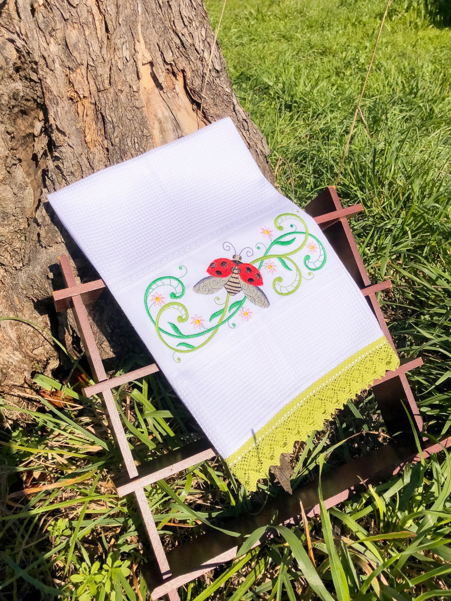 Toalha branca com bordado de joaninha sobre suporte de madeira na relva